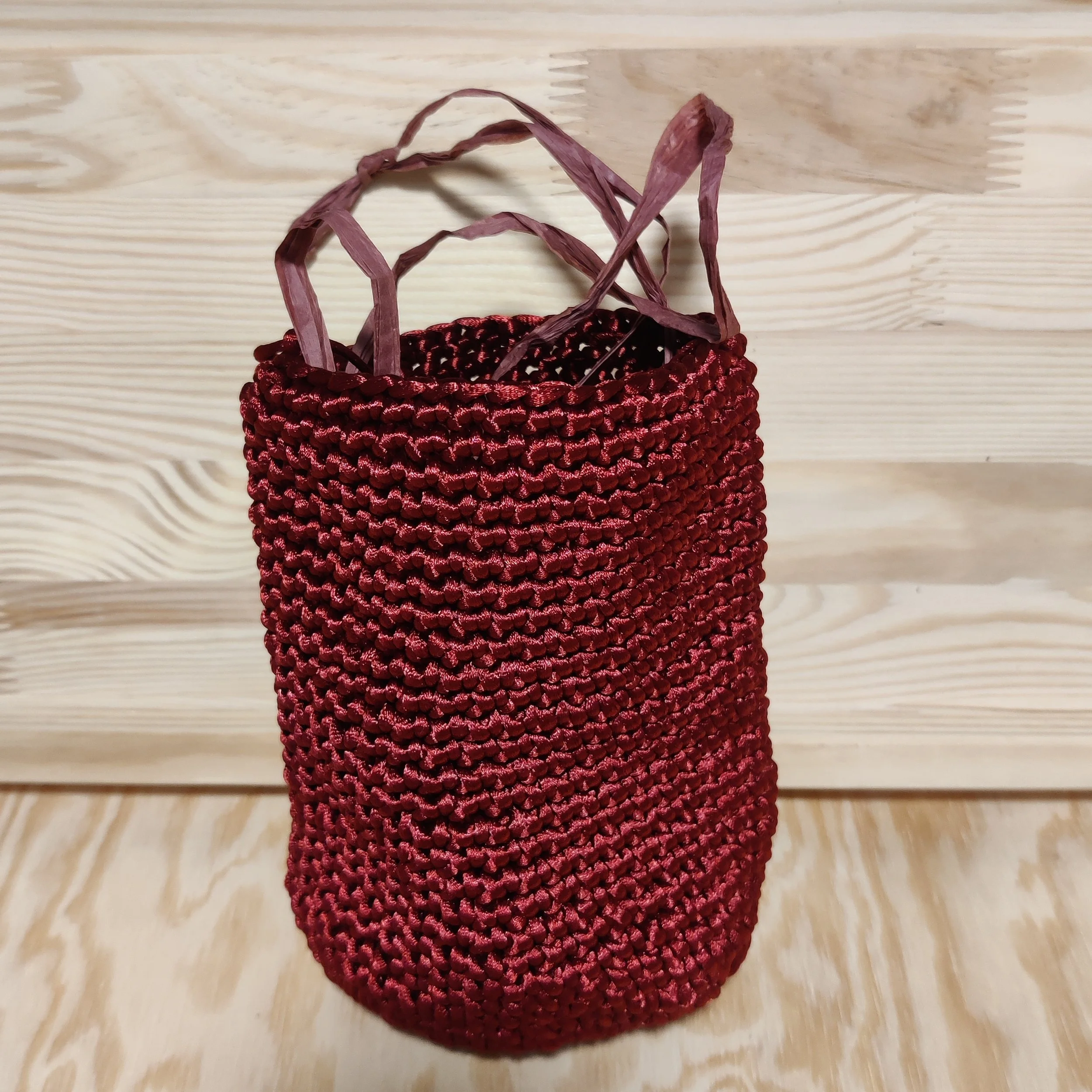 Cesta de cuerda trenzada de color burdeos con asas de cuerda más delgada, colocada sobre una superficie de madera clara.