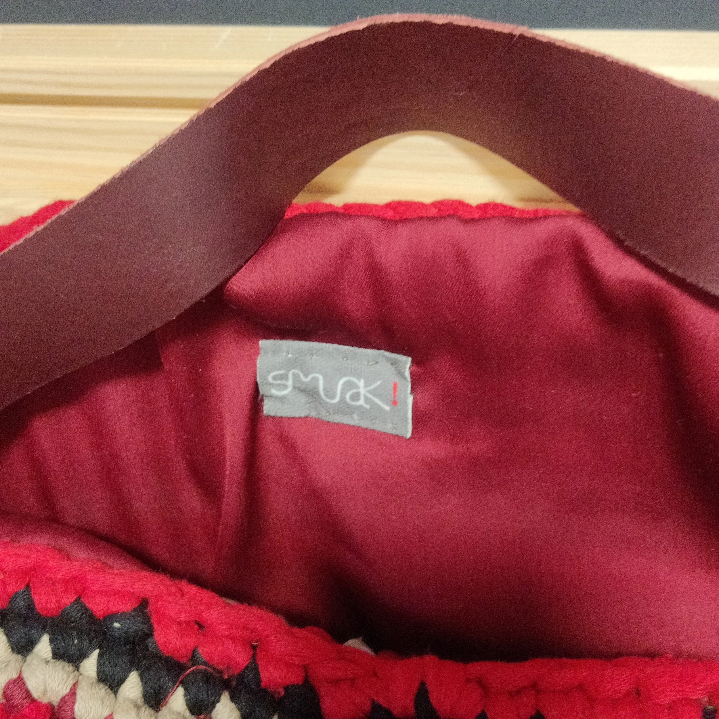 Interior de una bolsa con forro color rojo, con etiqueta gris que dice "smuak!" y una asa granate.