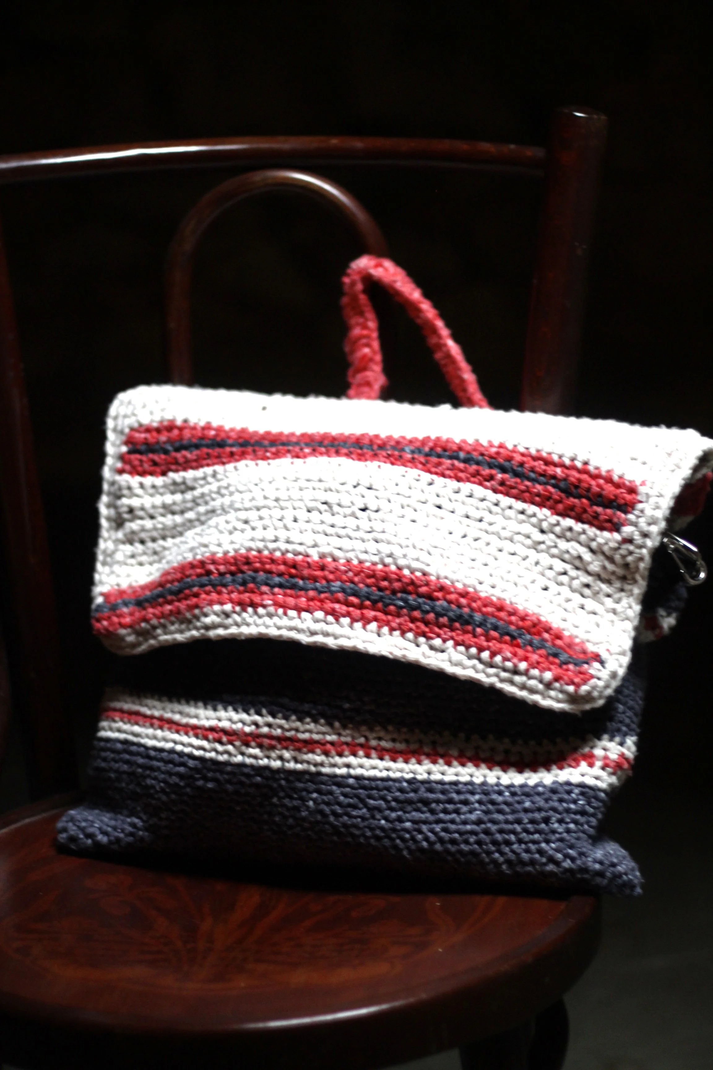 Bolso de mano tejido a crochet con rayas blancas, rojas y negras, colocado sobre una silla de madera.