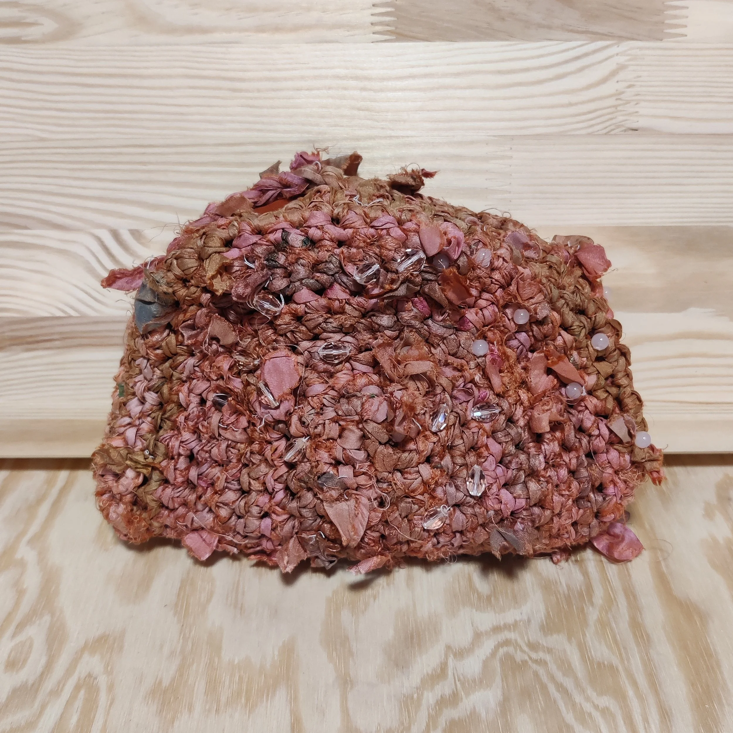 Cartera de mano para fiesta tejida en seda rosada y caldero con terminaciones del hilo al aire y cuentas de cristal cosidas por la superficie.