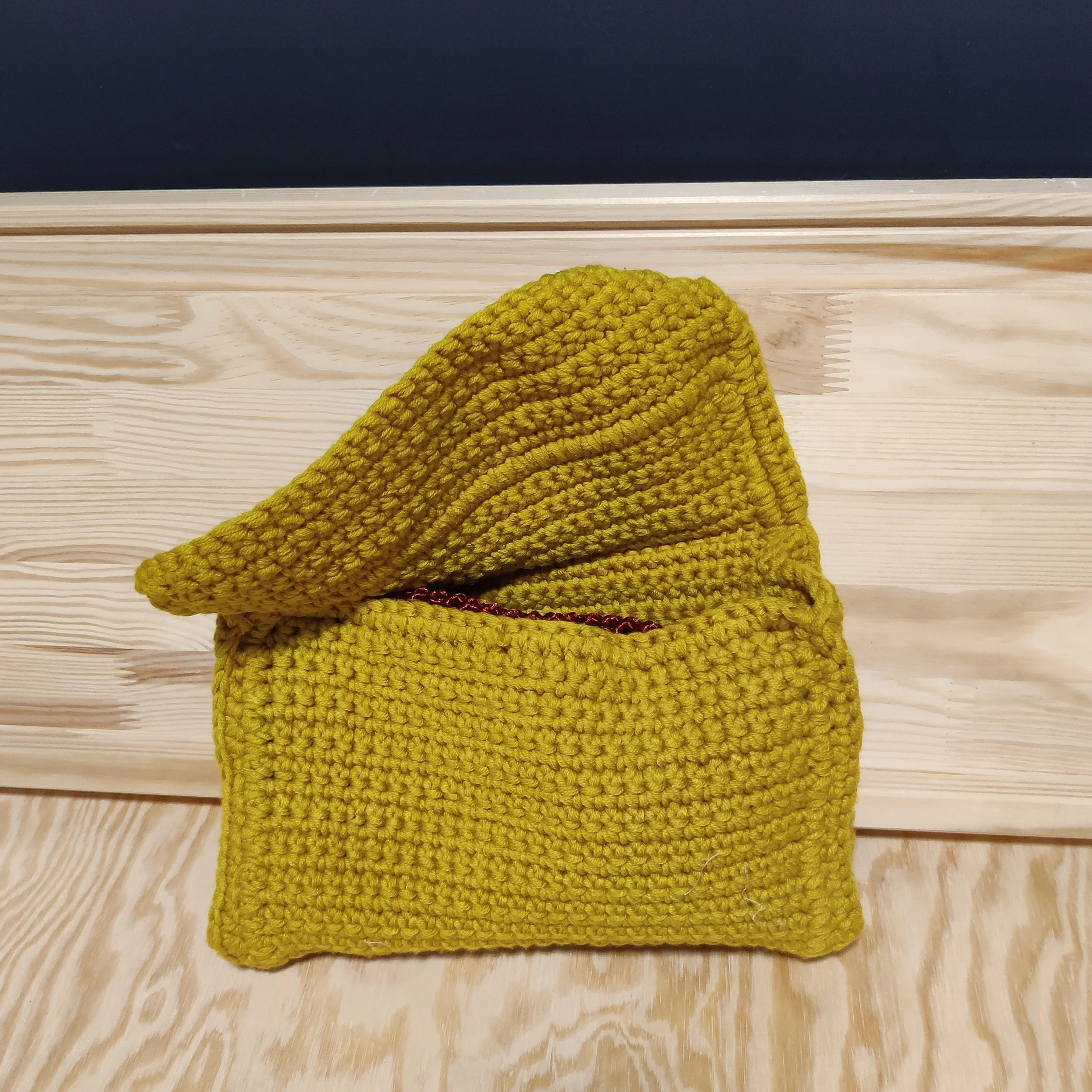 Bolso/cartera tejido en lana de color mostaza sobre una superficie de madera.