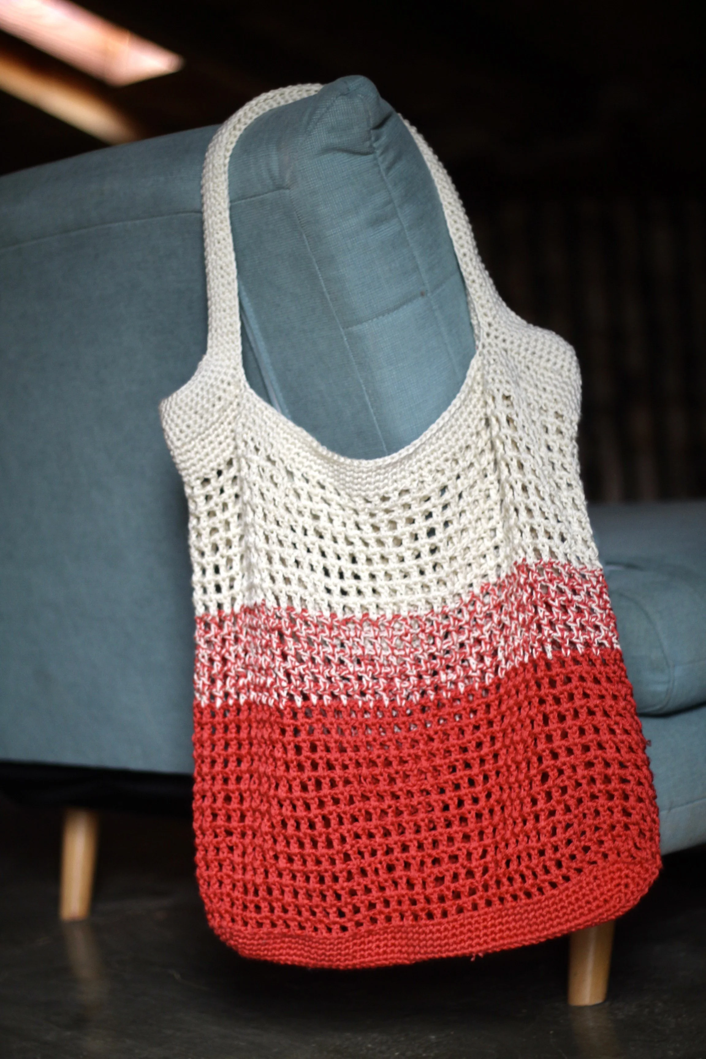 Bolso de crochet de color crudo y rojo colocado sobre un sofá azul.