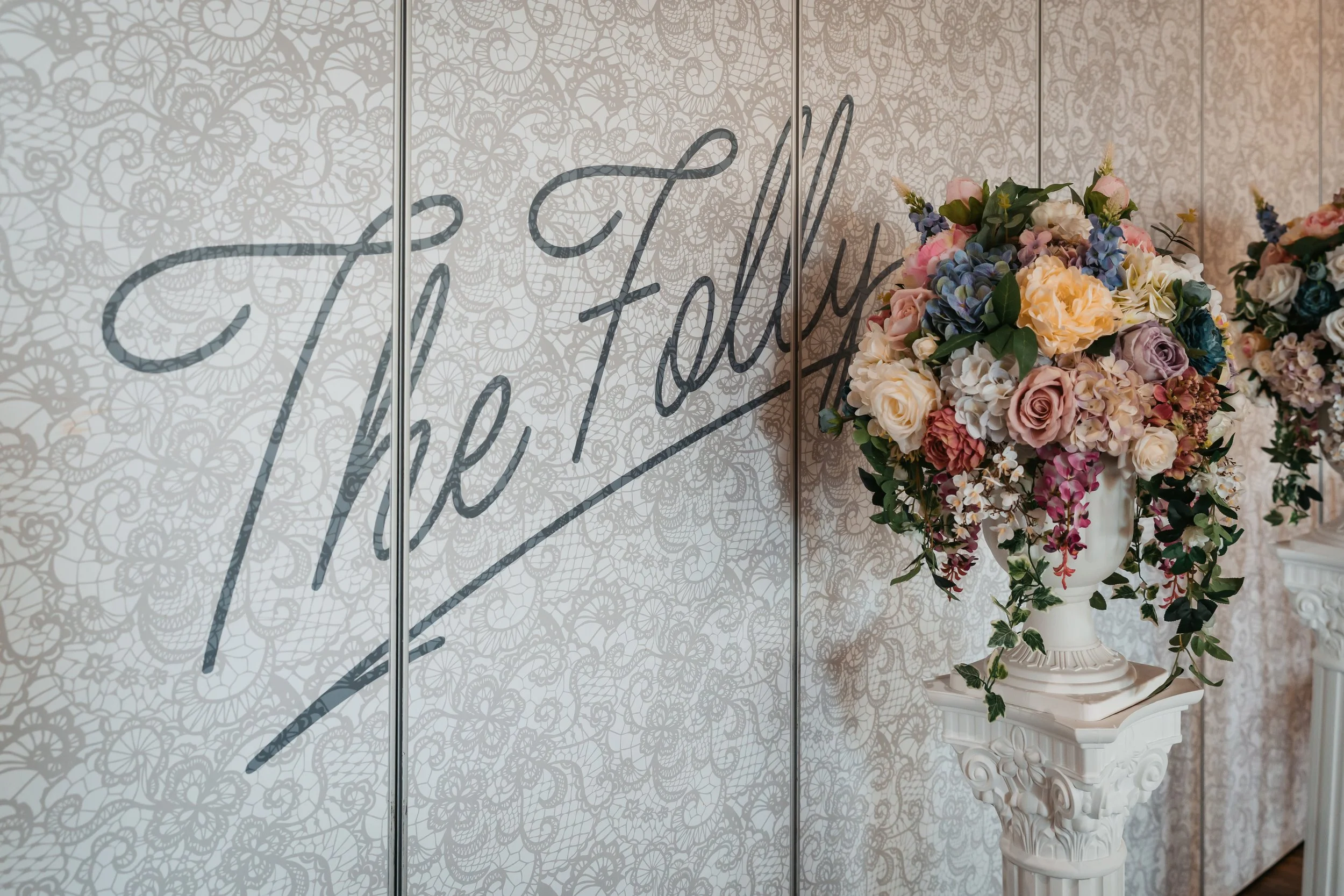 Decorative floral arrangement in a white vase on a white pedestal in front of a wall. Wedding decorations, Weddings in Derby, Wedding event.