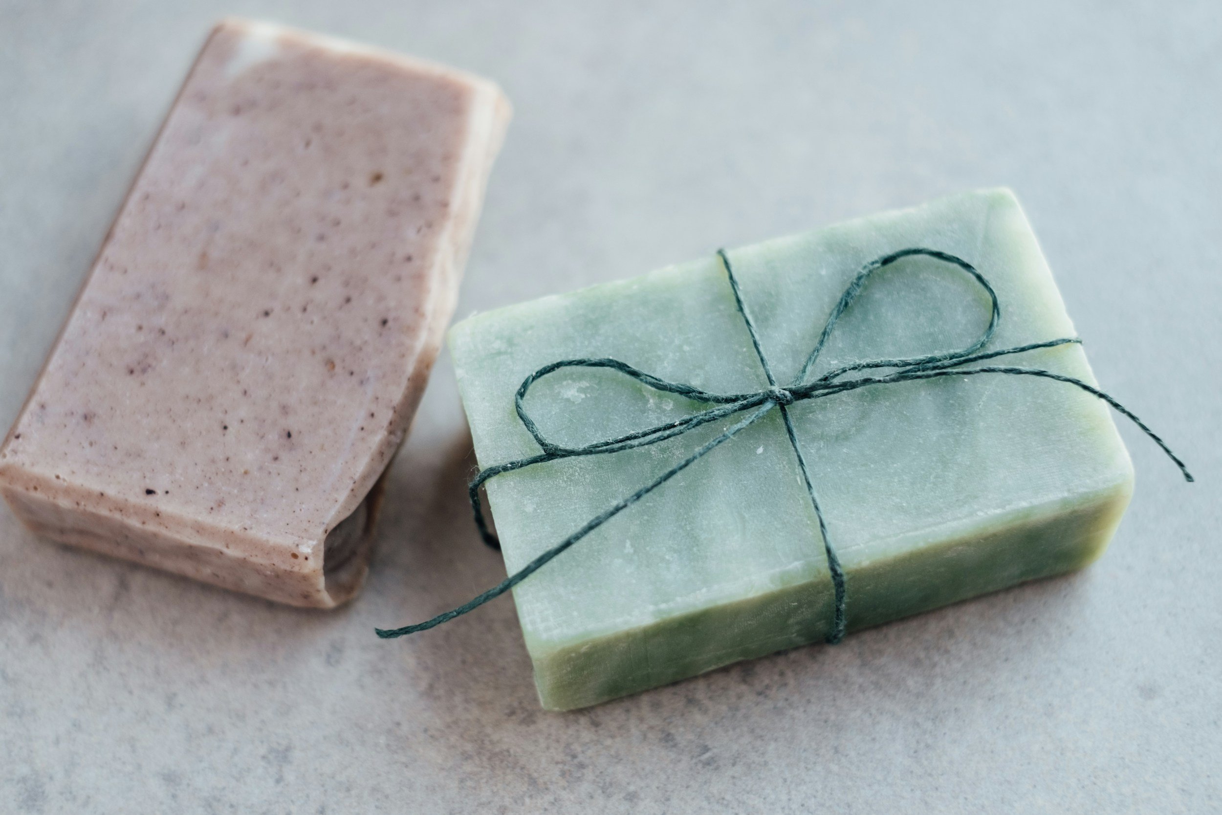 Two handmade soap bars, one beige with speckles, and one green tied with a green string.