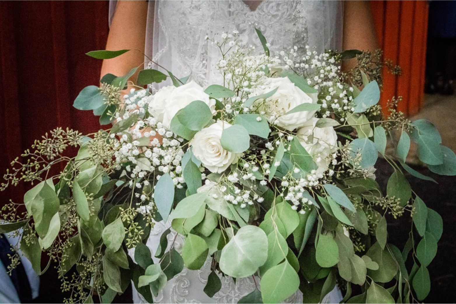 Elegant wedding bouquet with white roses, baby's breath, and eucalyptus leaves, held by a bride in a lace gown.