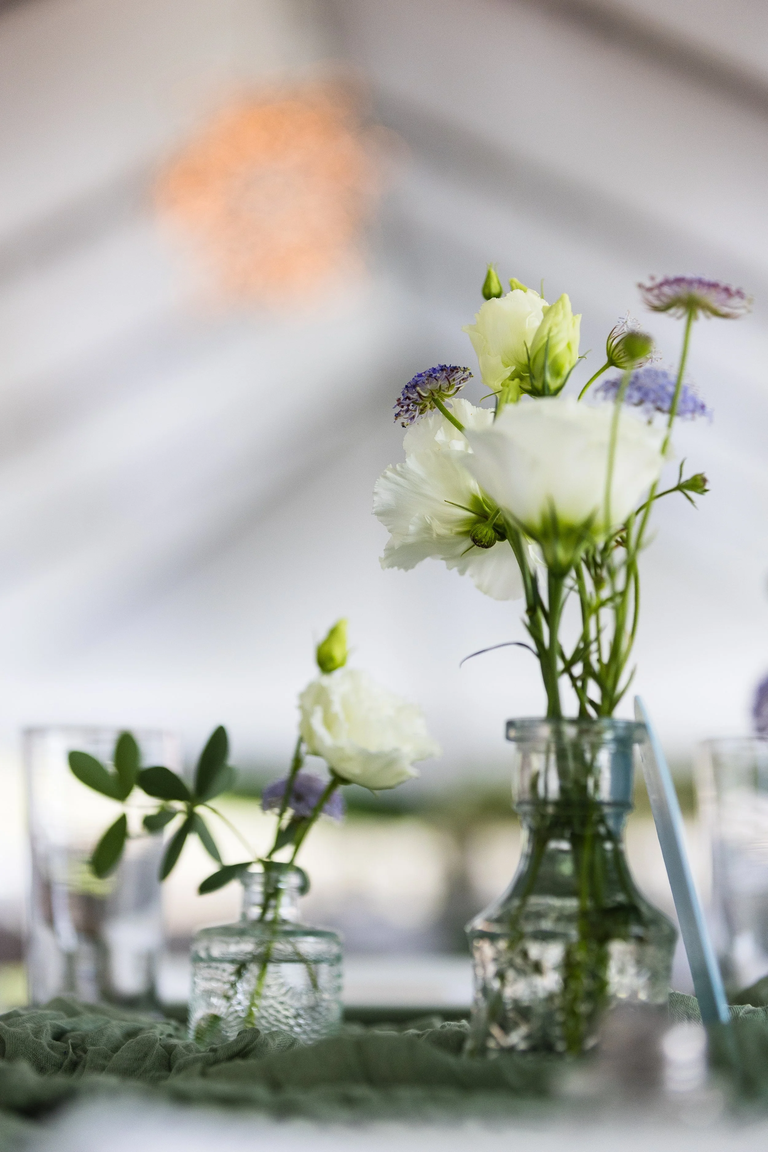 A close-up of a small floral arrangement with white and purple flowers in glass jars on a table.