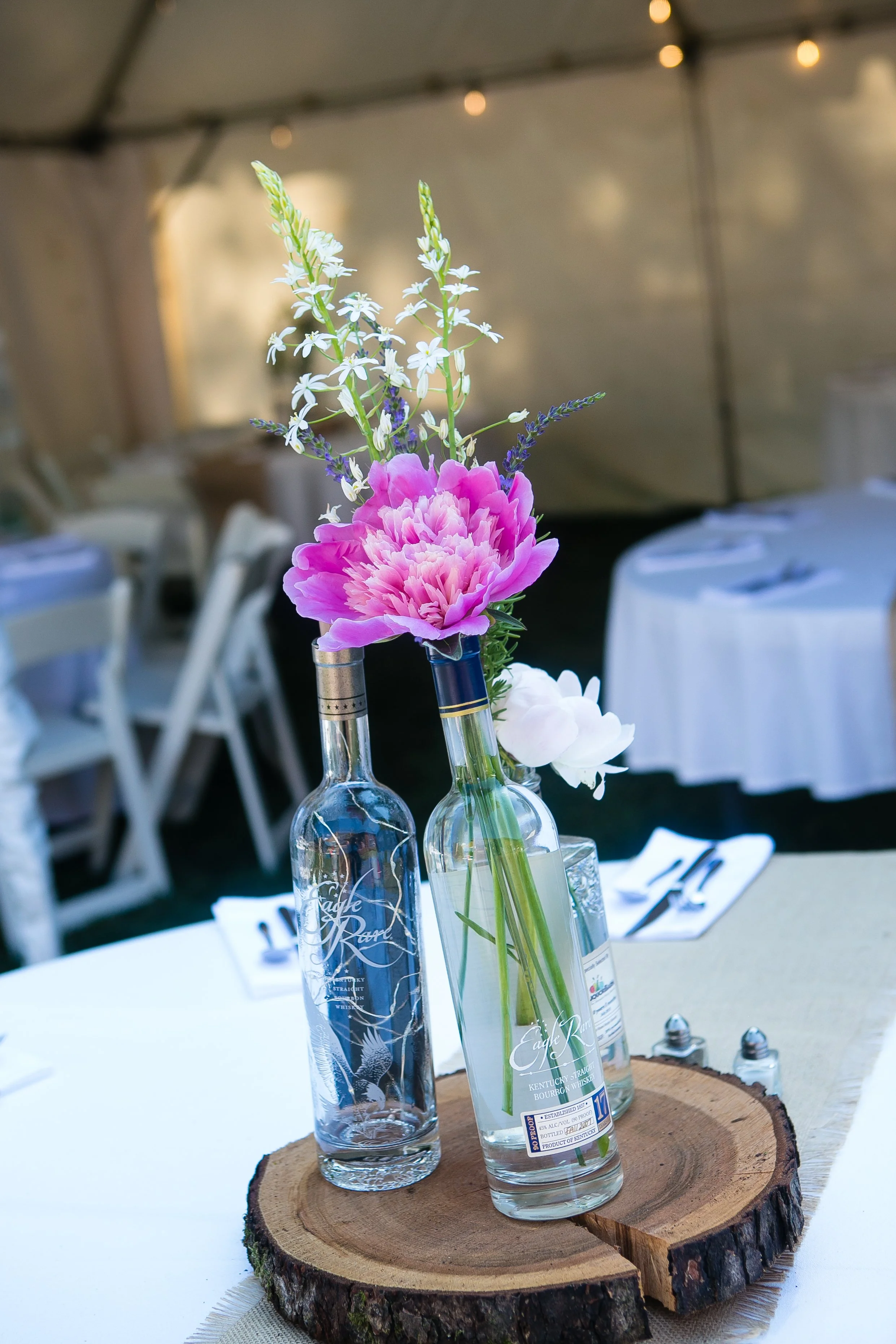 Arrangement of flowers in glass bottles on a wood slice at a dining event.