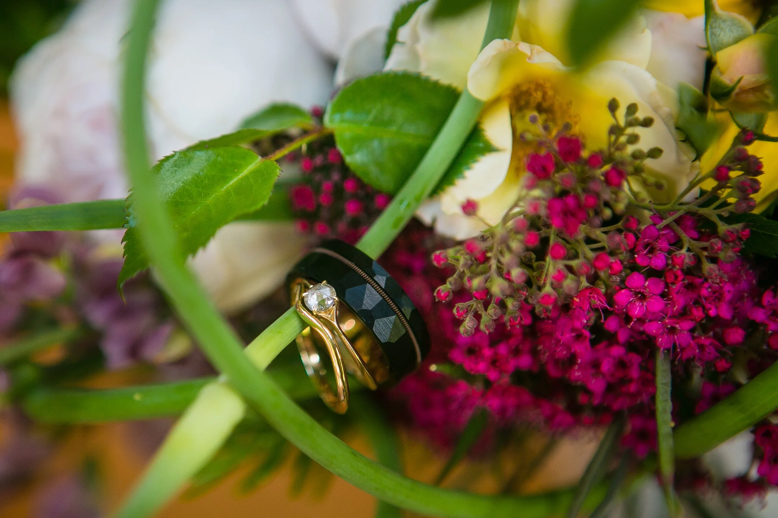 A wedding bouquet with white and purple flowers, green leaves, and rings placed on a green stem.