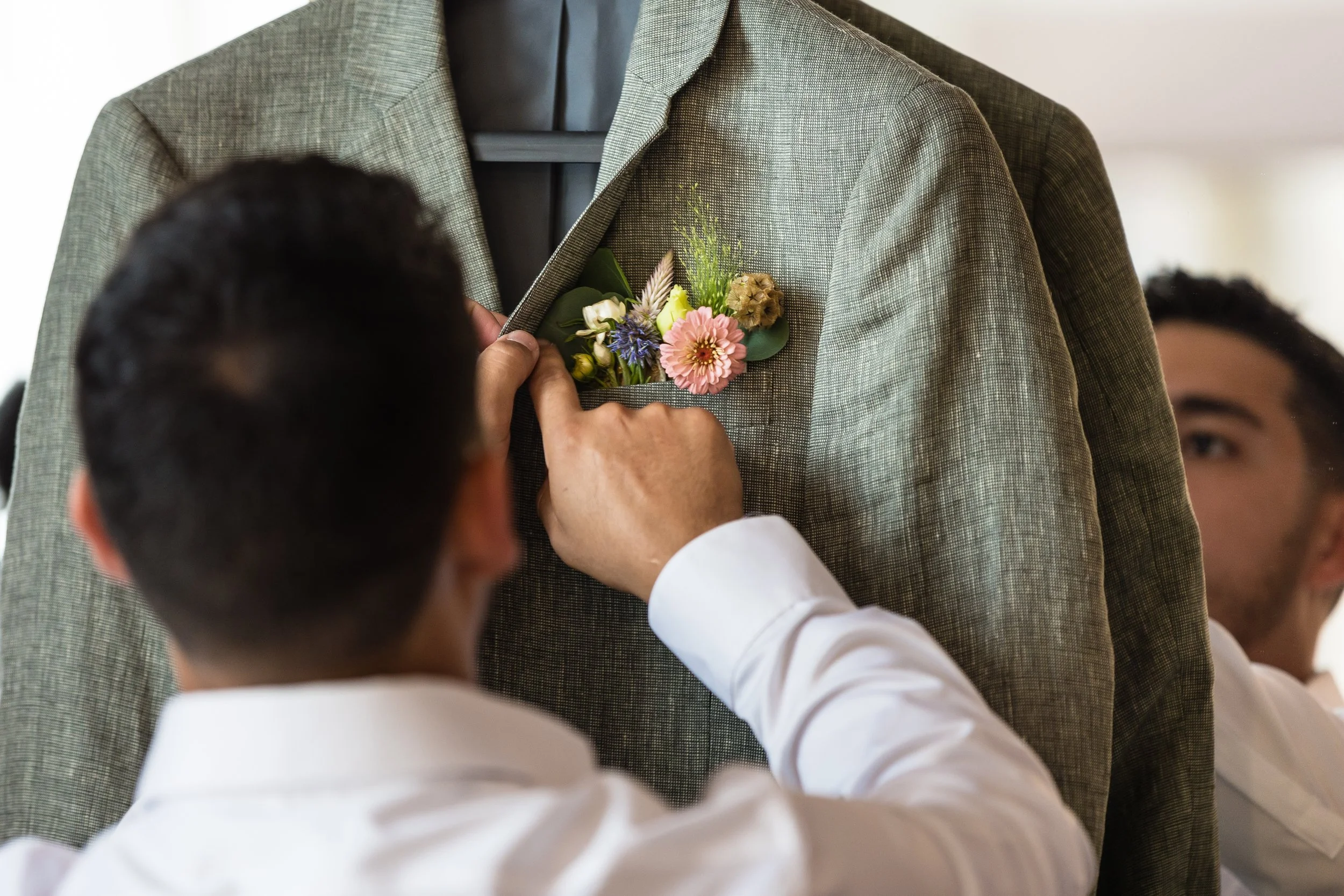 A person pinning a colorful boutonniere to a gray suit jacket.
