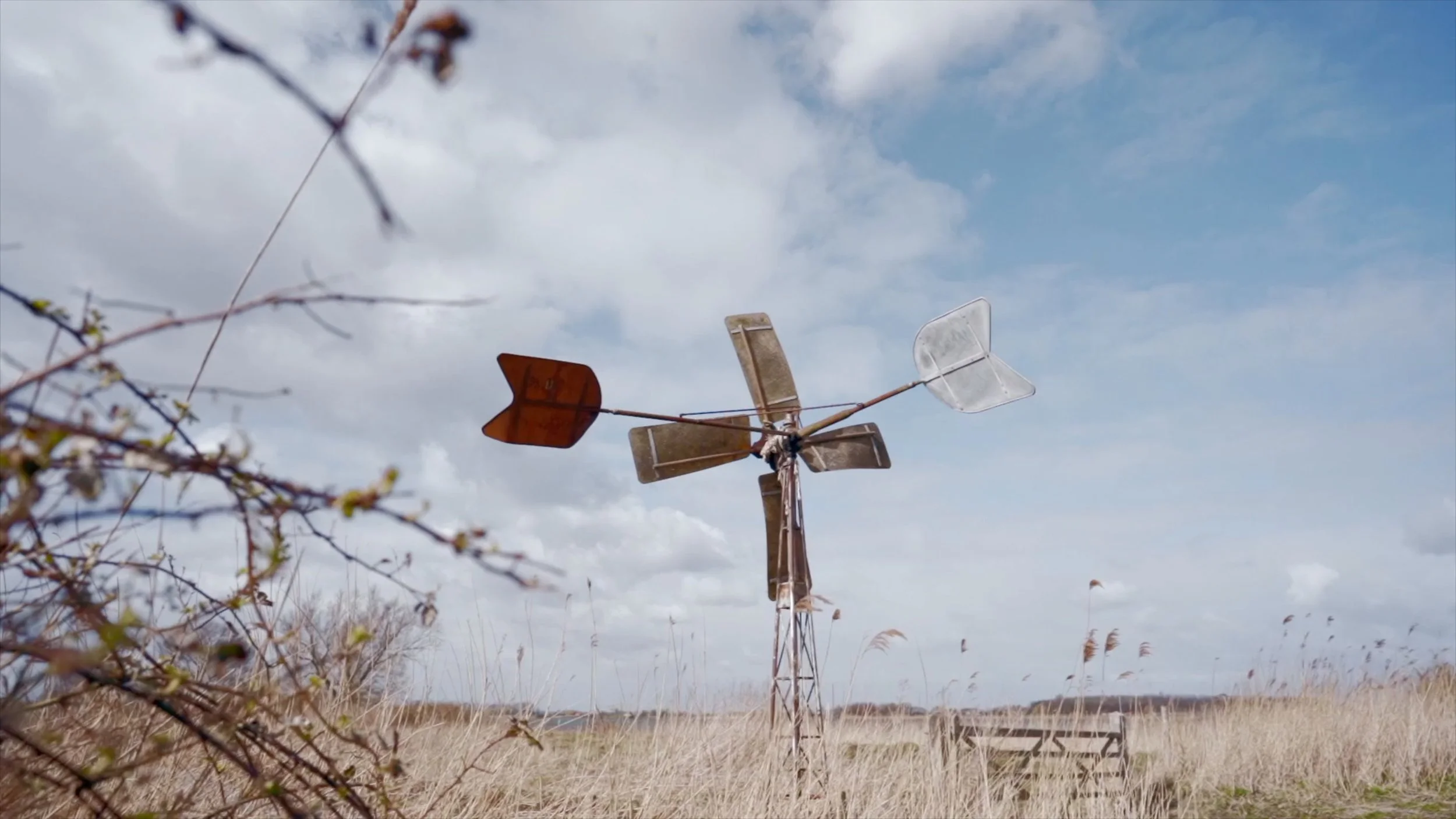 Rusty, weathered windmill in tall grass under cloudy sky.