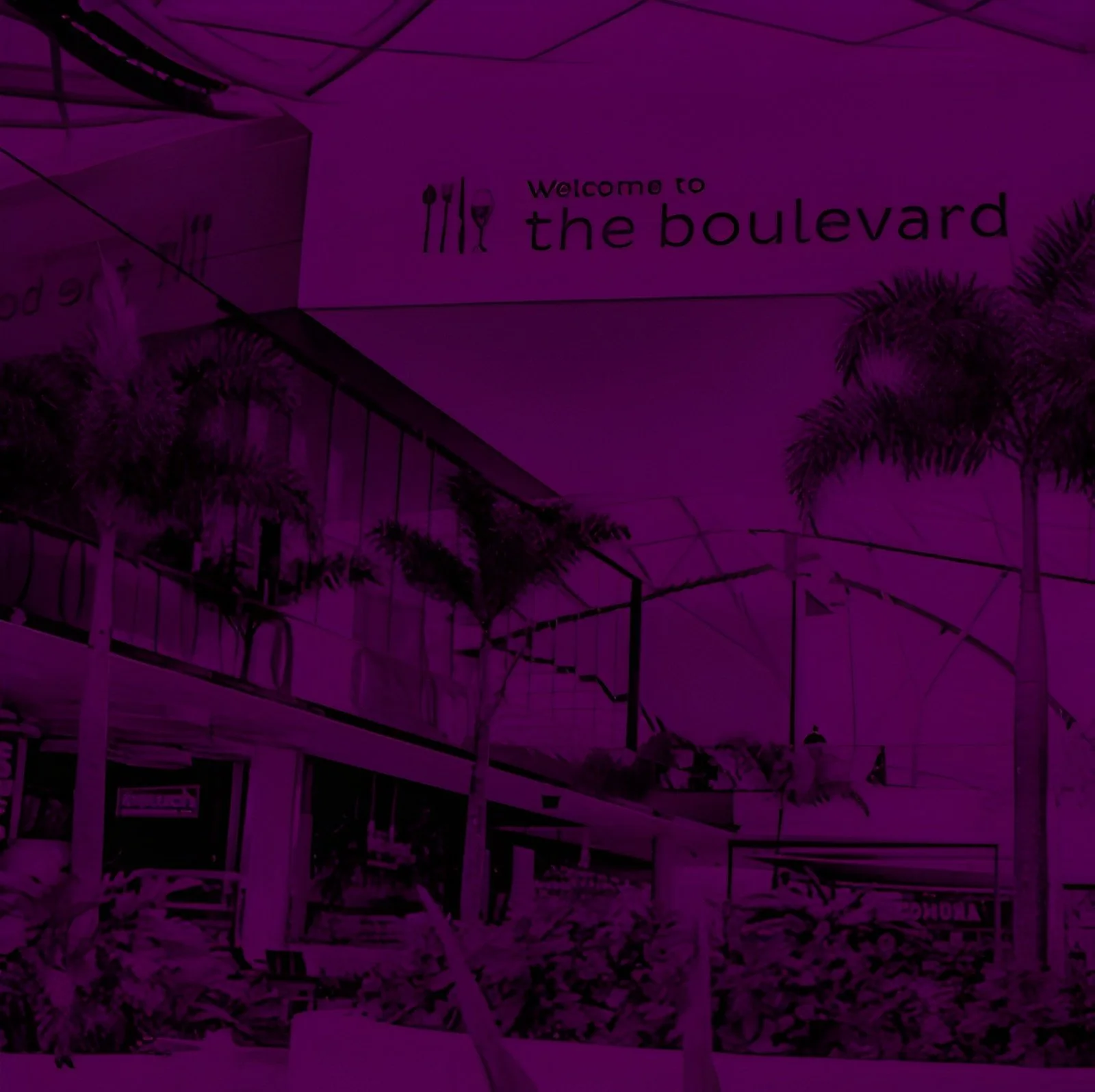Sign that says 'Welcome to the boulevard' with illustrations of cutlery and a glass of wine, in an outdoor shopping area with palm trees.
