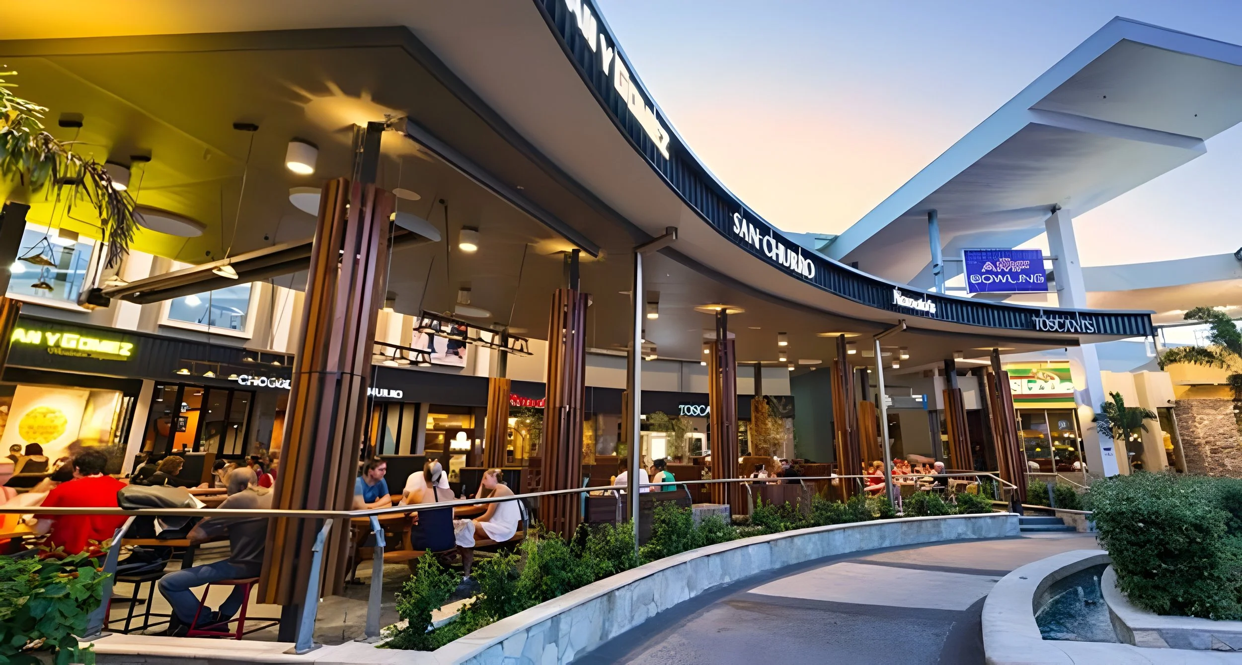 Outdoor shopping mall with various eateries and shops, people sitting at tables, modern architecture, and greenery around.