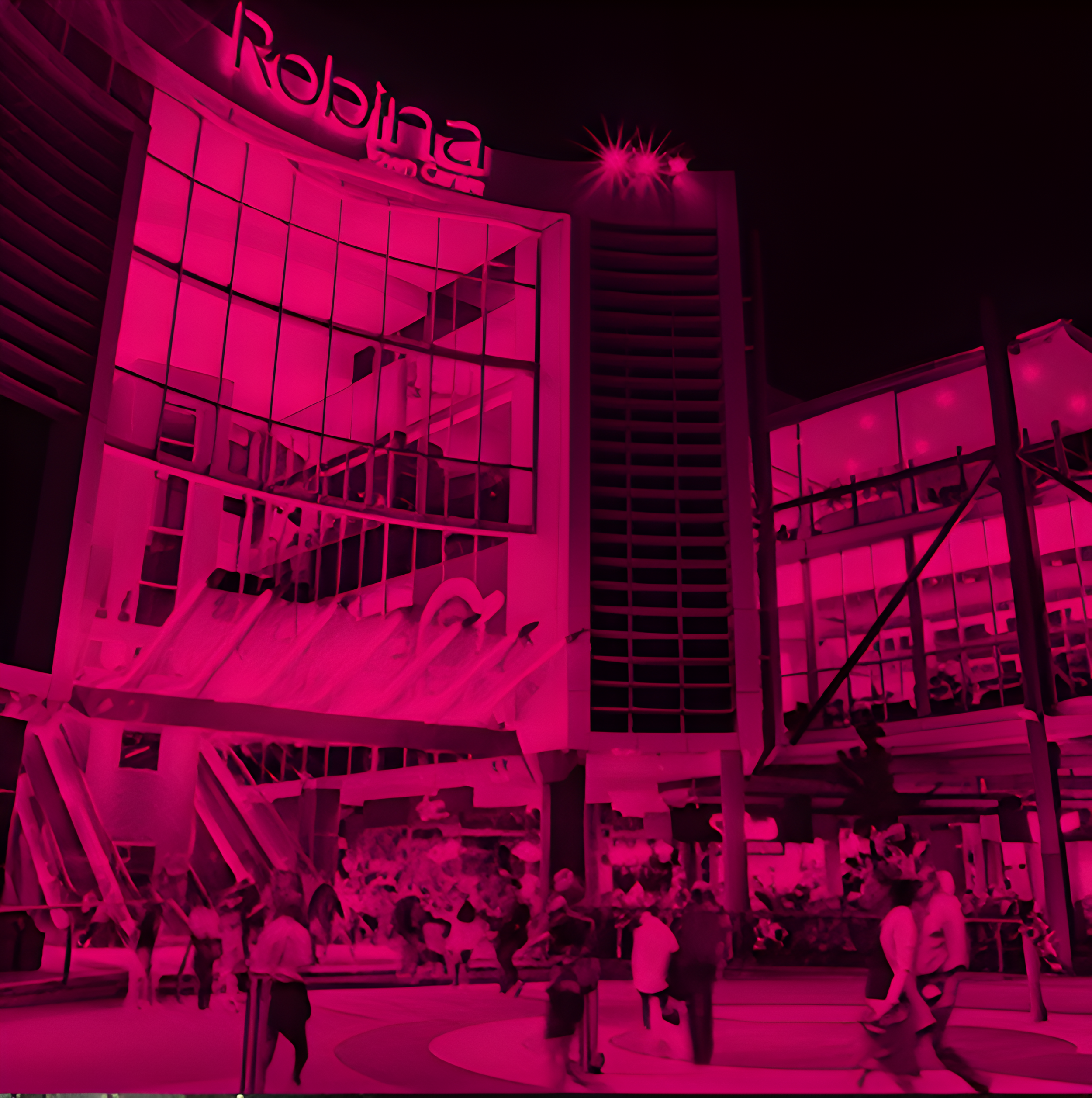 Night view of a modern building with large glass windows displaying the Radisson logo, illuminated with pink lighting, with people walking and gathering outside.