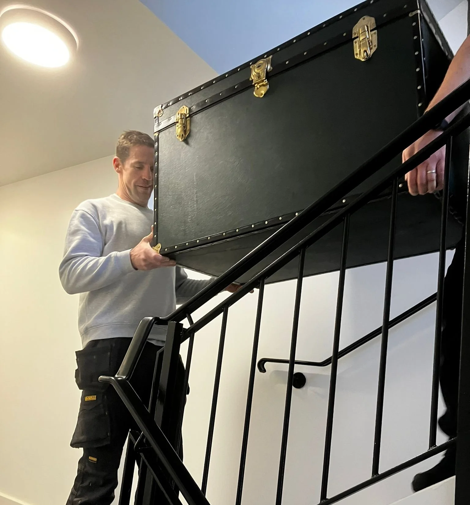 Two men from Your Move Mate carrying a large black case up a staircase indoors.