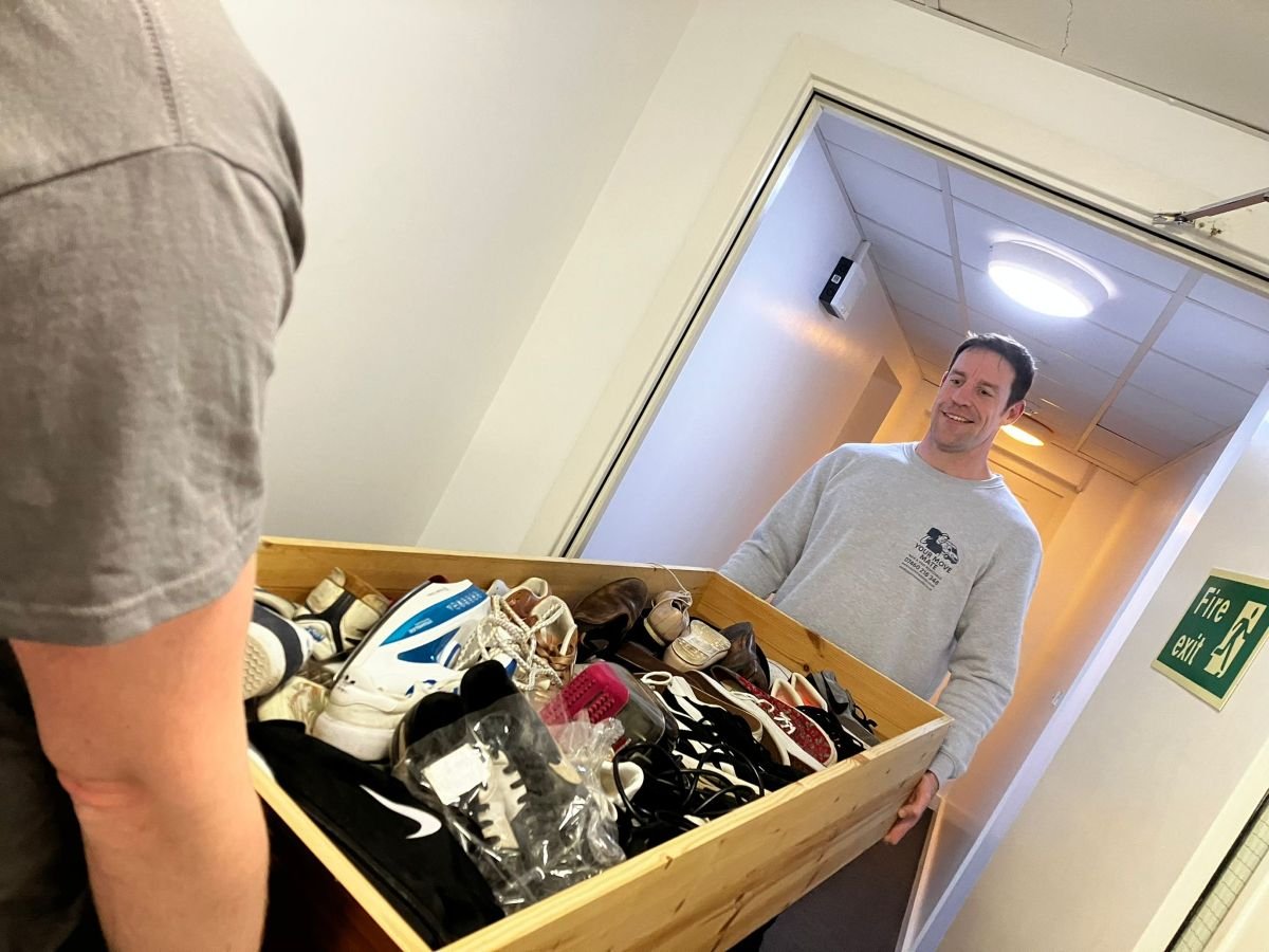 Don smiling while holding a large wooden box filled with assorted shoes in a student halls move