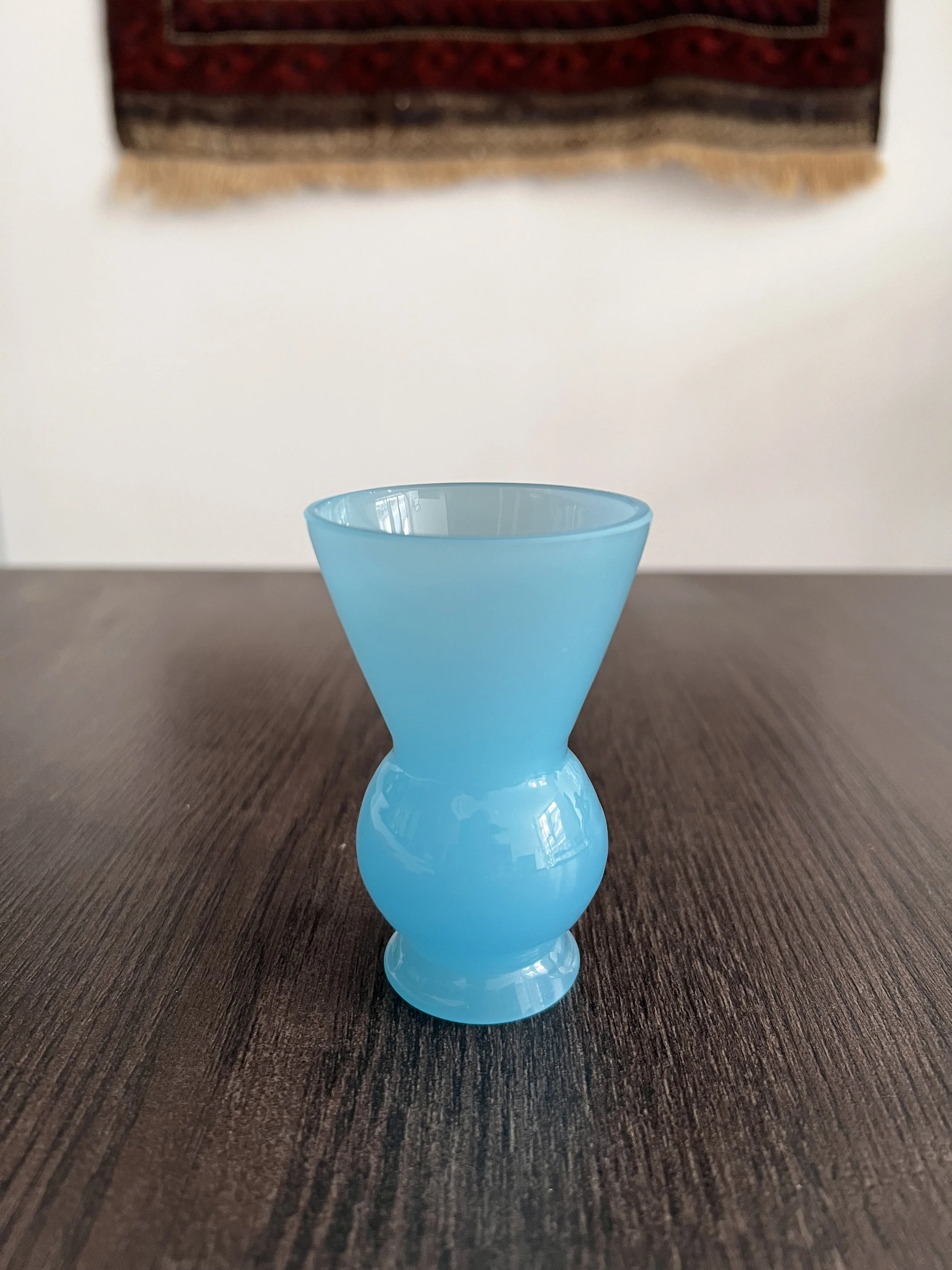 Small mid-century vintage baby blue opaline glass vase with a flared trumpet neck, bulbous spherical base, and short pedestal foot, displayed on a dark wooden table background.