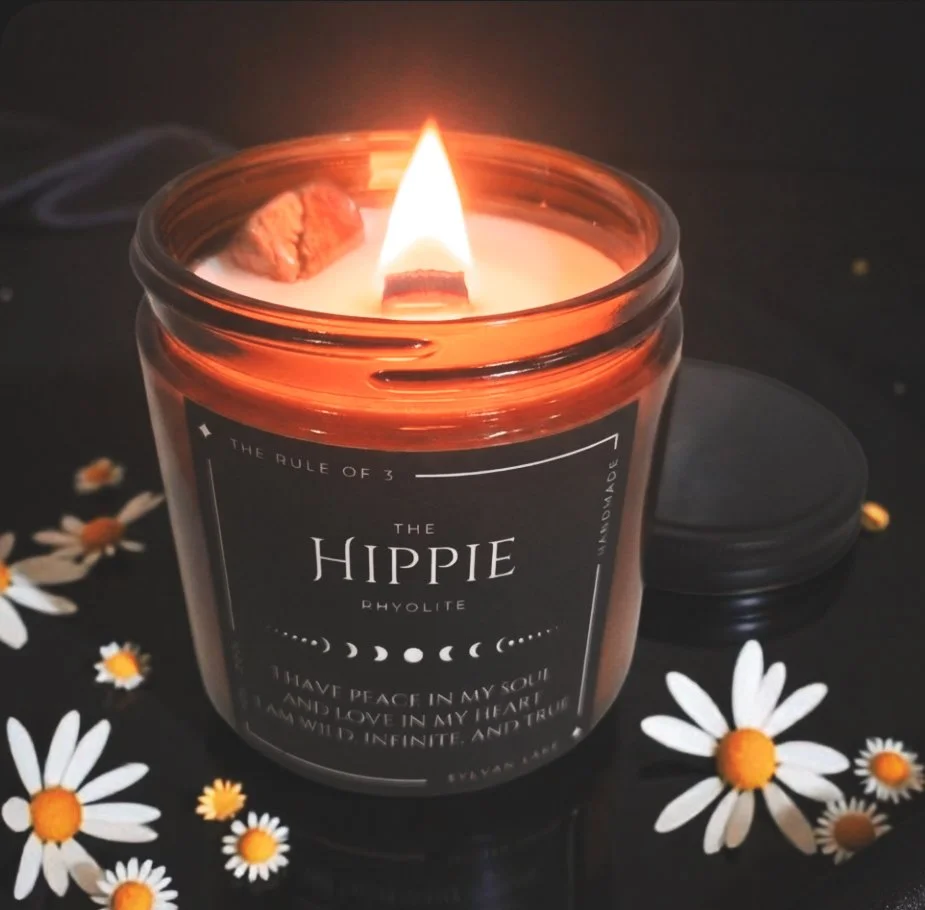 “Lit Hippie ritual candle with a crackling wood wick, styled with scattered daisies on a dark background.”