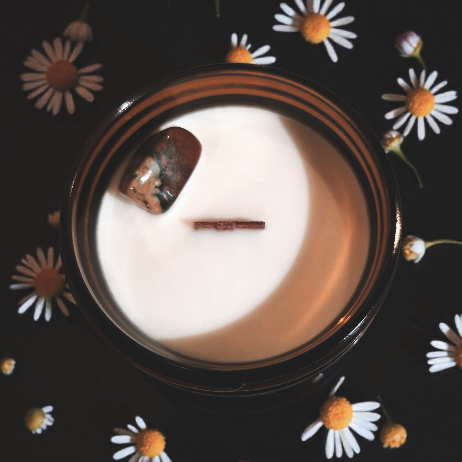 “Top view of The Hippie candle showing the wood wick and rhyolite crystal, styled with daisies.”
