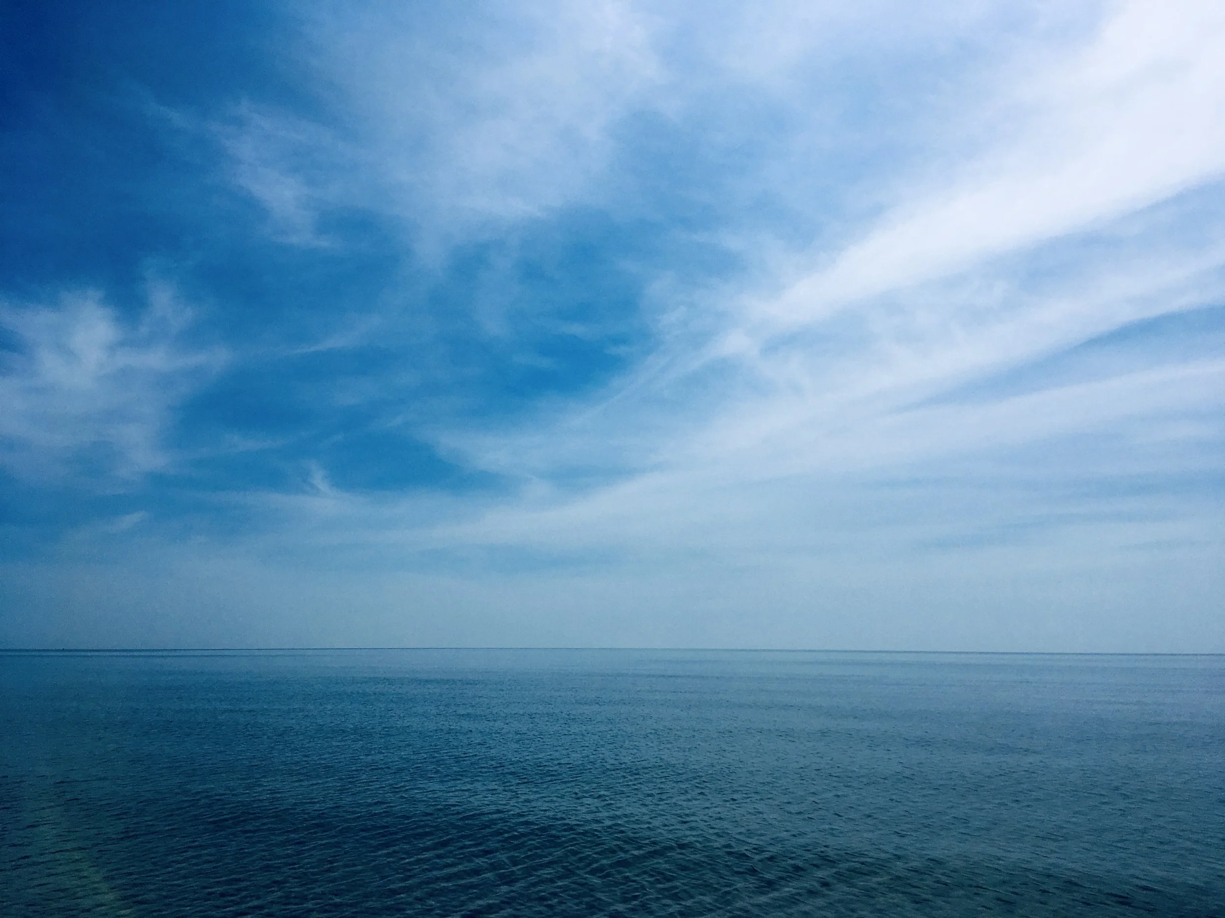 Calm ocean with a clear blue sky and wispy clouds.