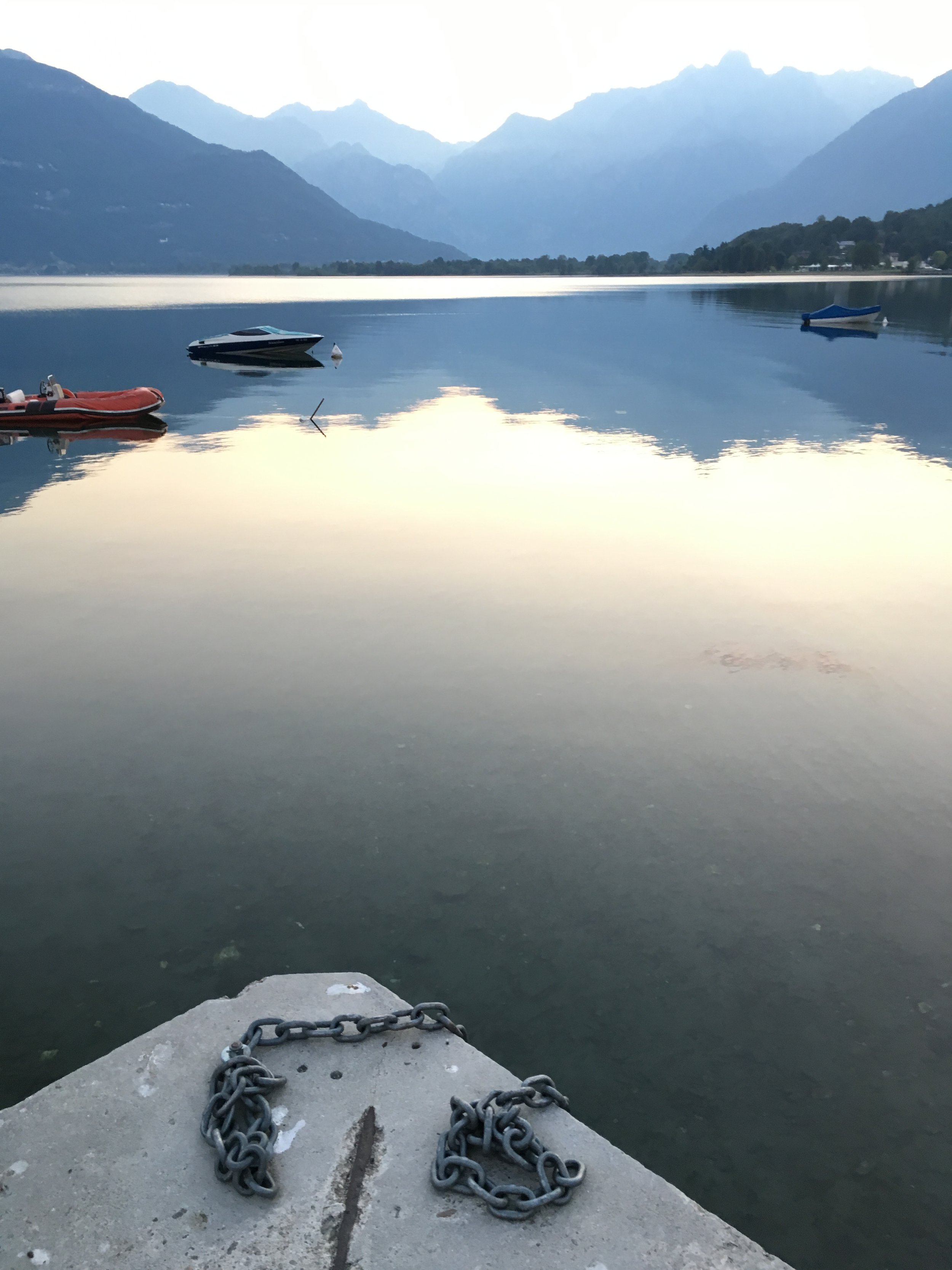 Calm lake with three boats and a chain in the foreground, surrounded by mountains in the distance