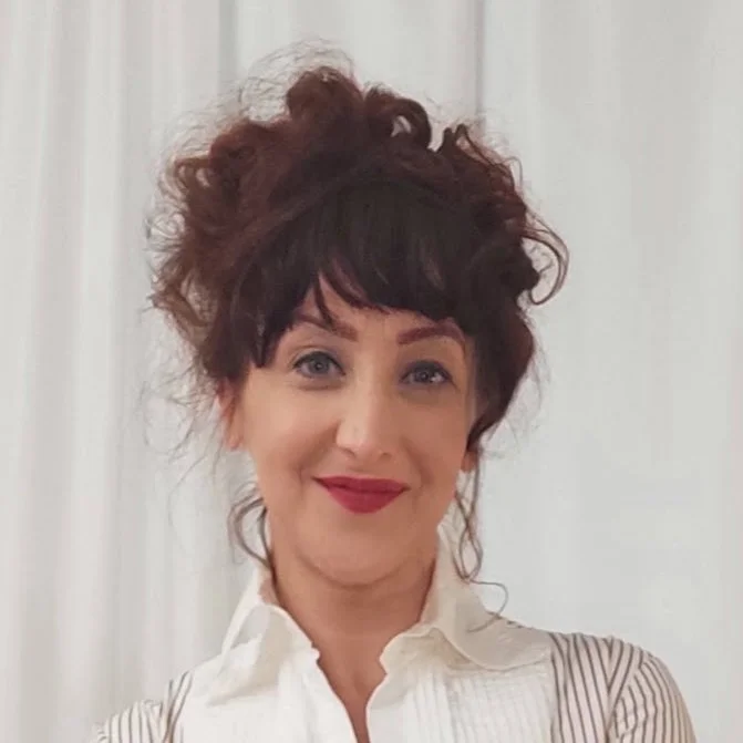A woman with dark hair piled into an updo with  a bright smile standing against a white background