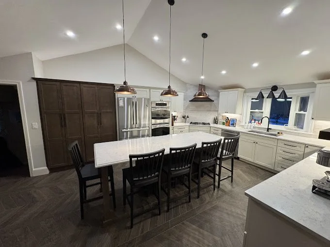 Modern kitchen with white cabinets, a large island with seating, stainless steel appliances, pendant lighting, and a window above the sink.