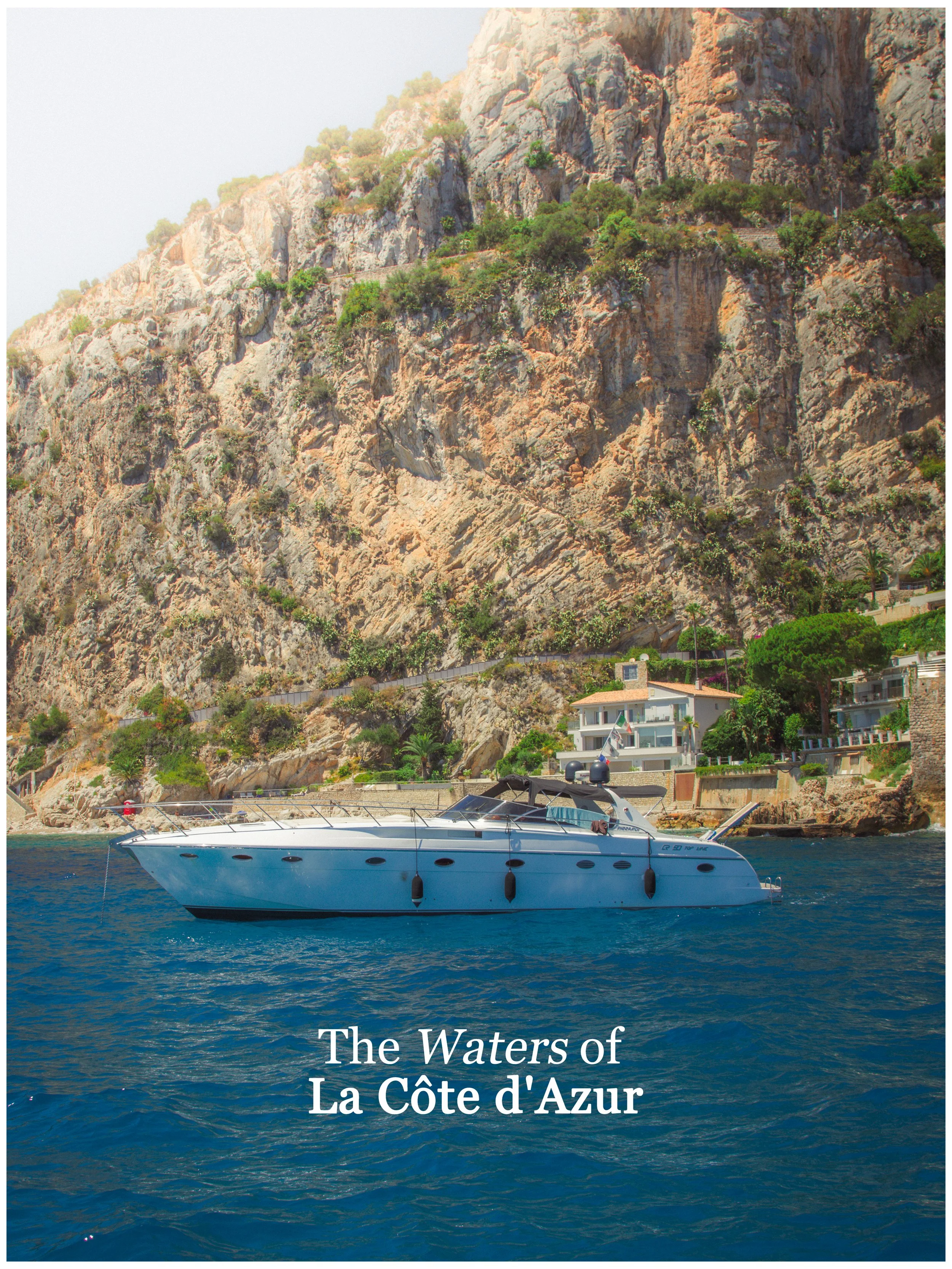 A yacht floating on the sea near a rocky coastline with houses and greenery in La Côte d'Azur.