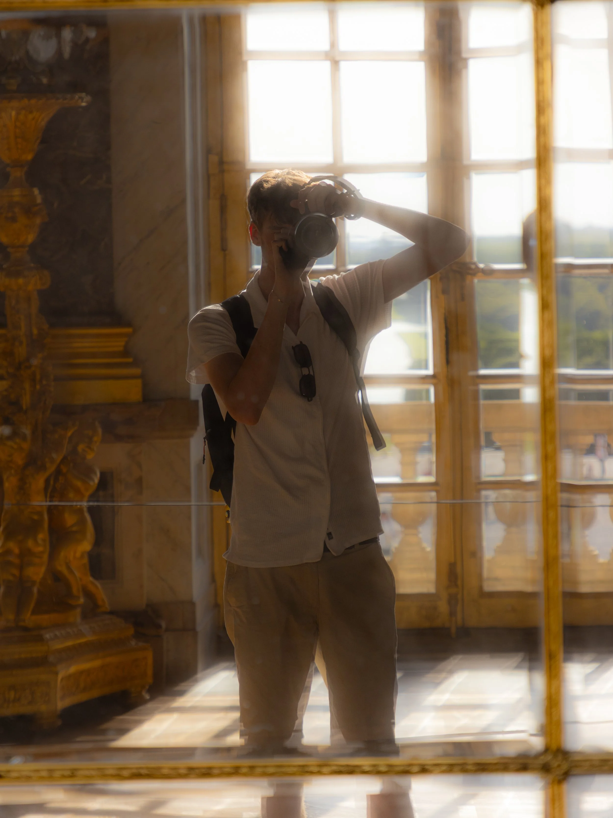 Person taking a photo in a historic or elegant room with large windows and ornate gold details.