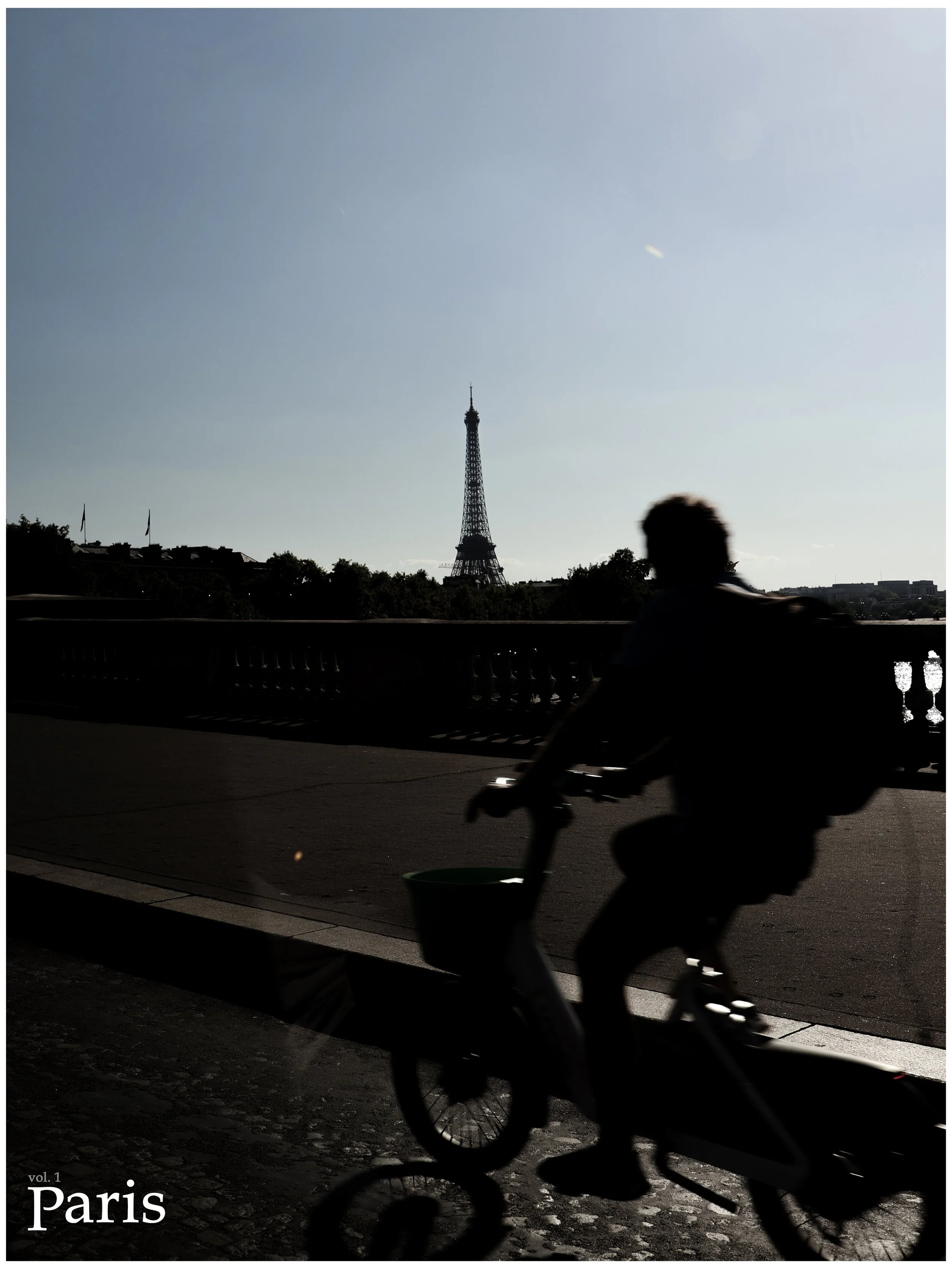 Silhouette of a person riding a bicycle along a bridge in Paris with the Eiffel Tower in the background during daylight.