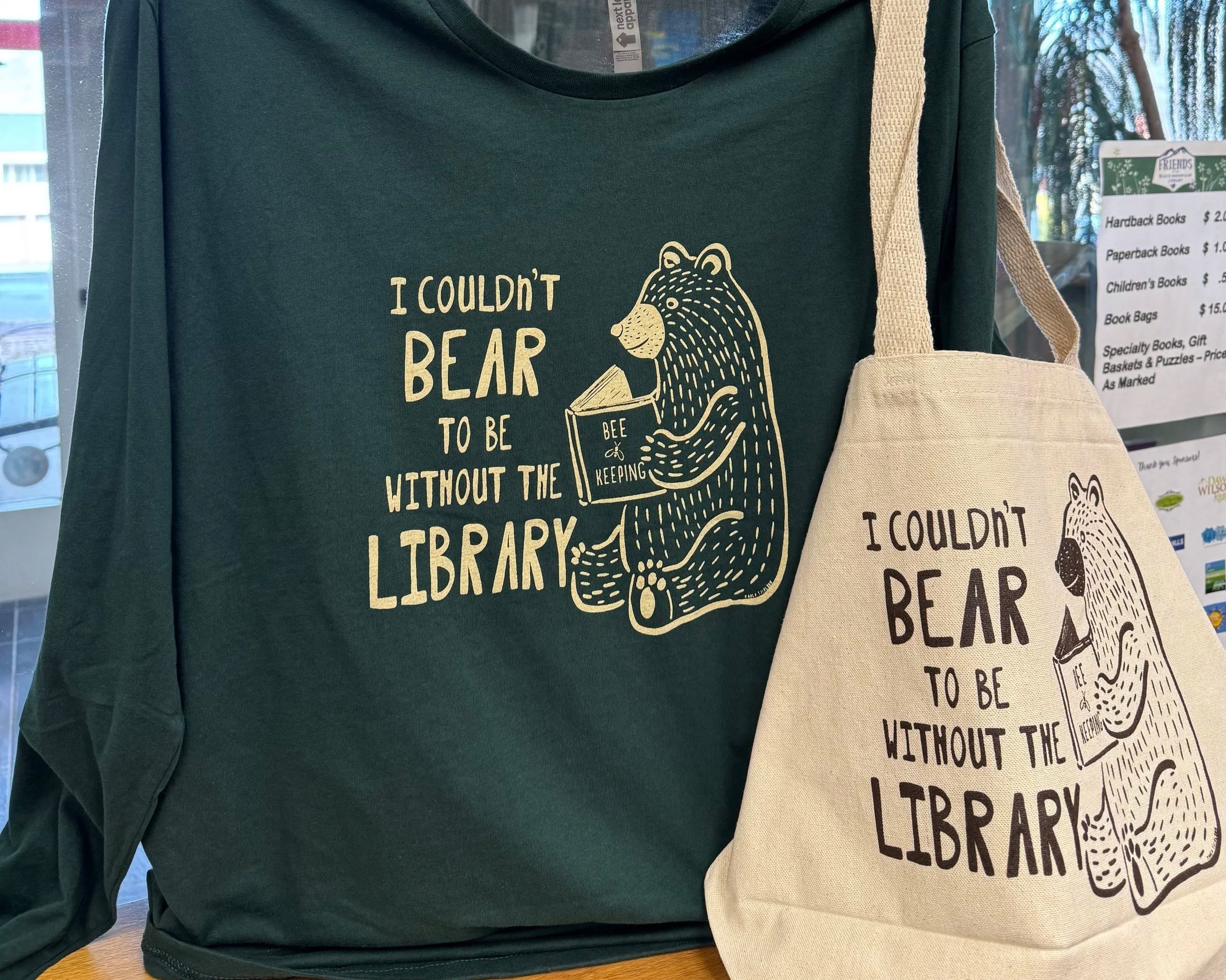 Two tote bags with cityscape line art designs for Buncombe County Public Libraries, one in black and white, the other in red and white.