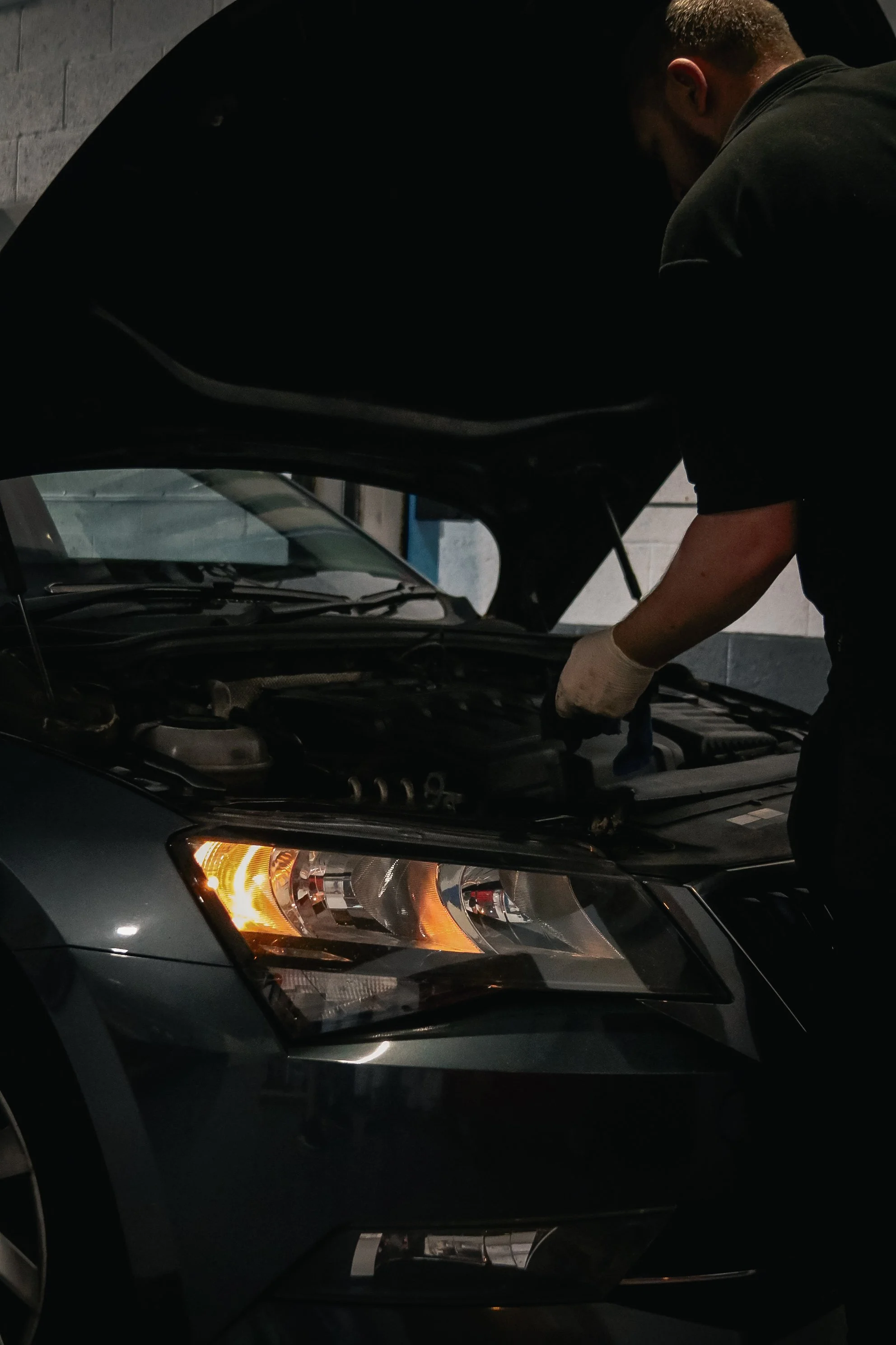 A mechanic working under the open hood of a car inside a garage.
