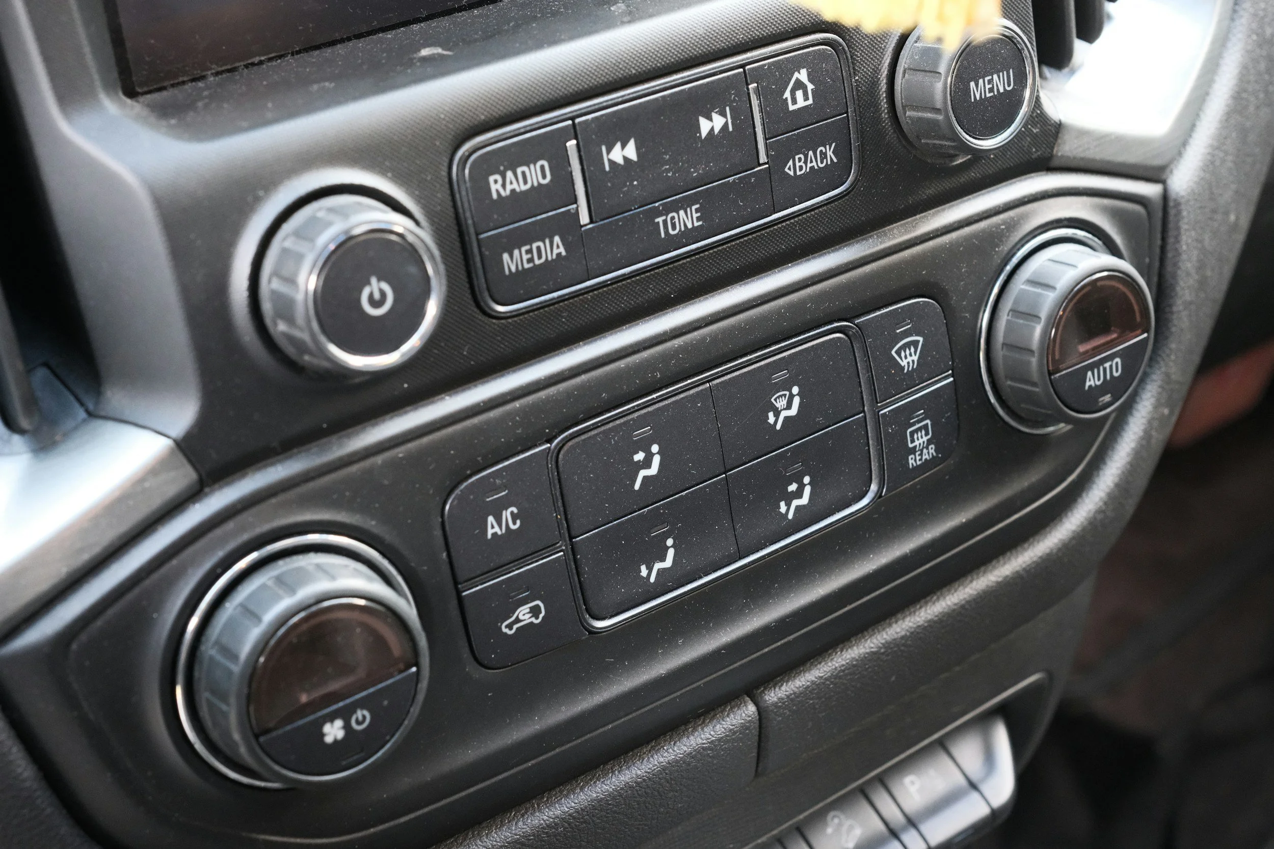 Car dashboard controls including climate control dials, air conditioning, rear defrost, air circulation, and audio system buttons.