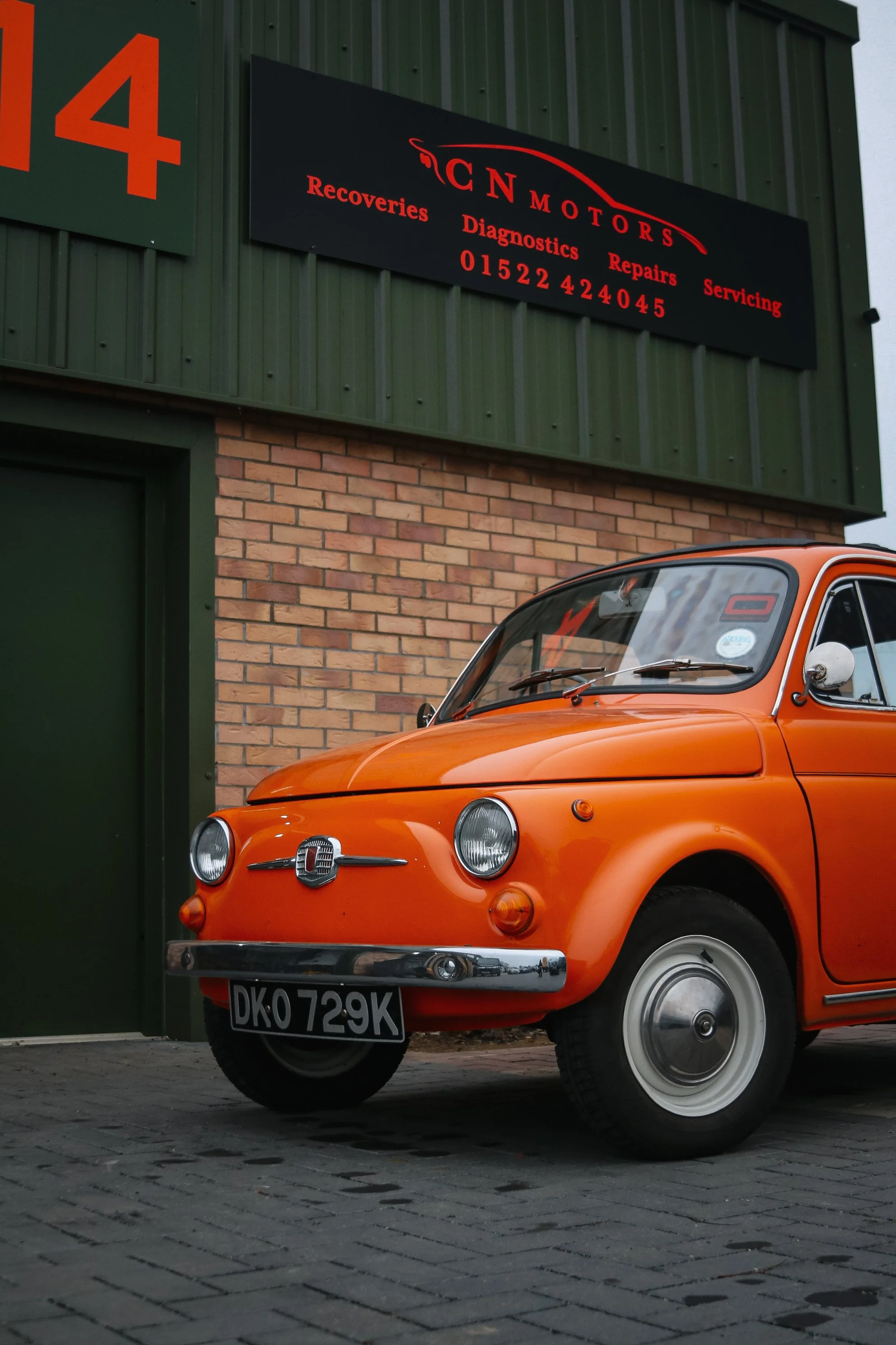 An orange vintage Fiat 500 parked outside a garage with a sign for CN Motors