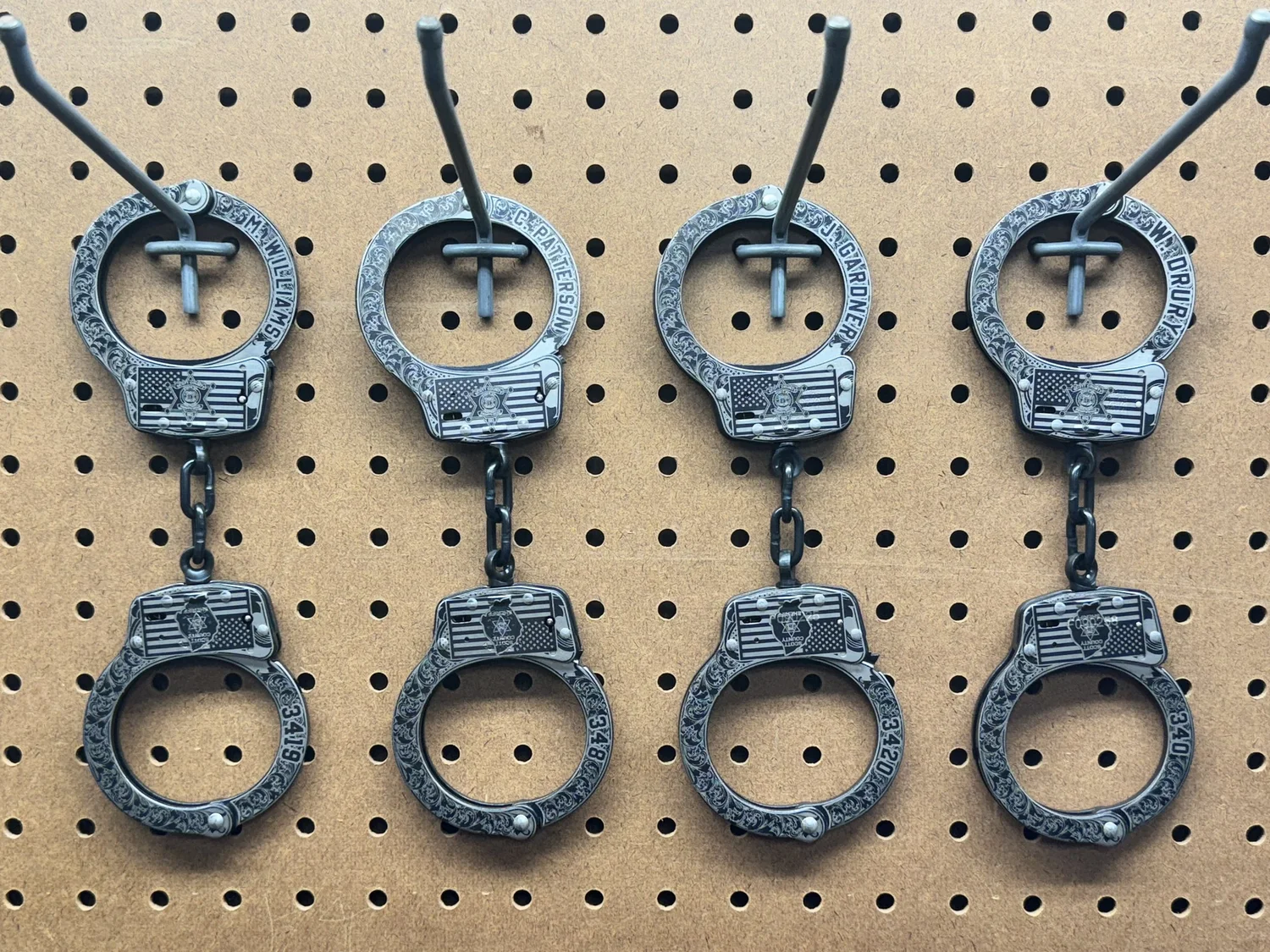 Engraved handcuffs displayed on a shop pegboard