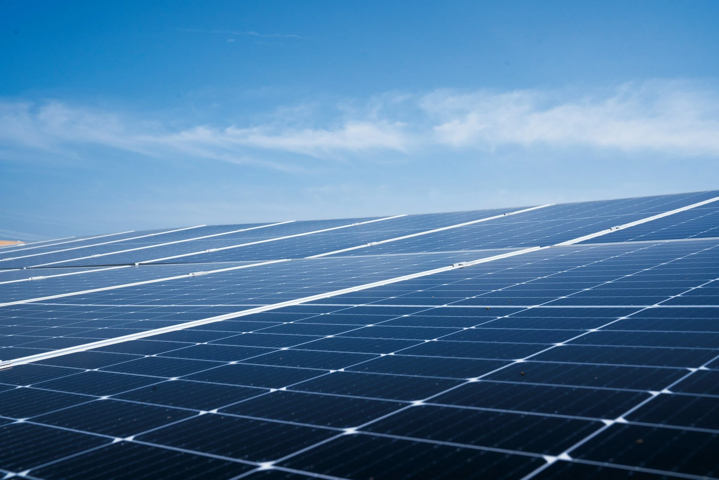 A large array of solar panels installed outdoors under a bright blue sky with a few clouds.