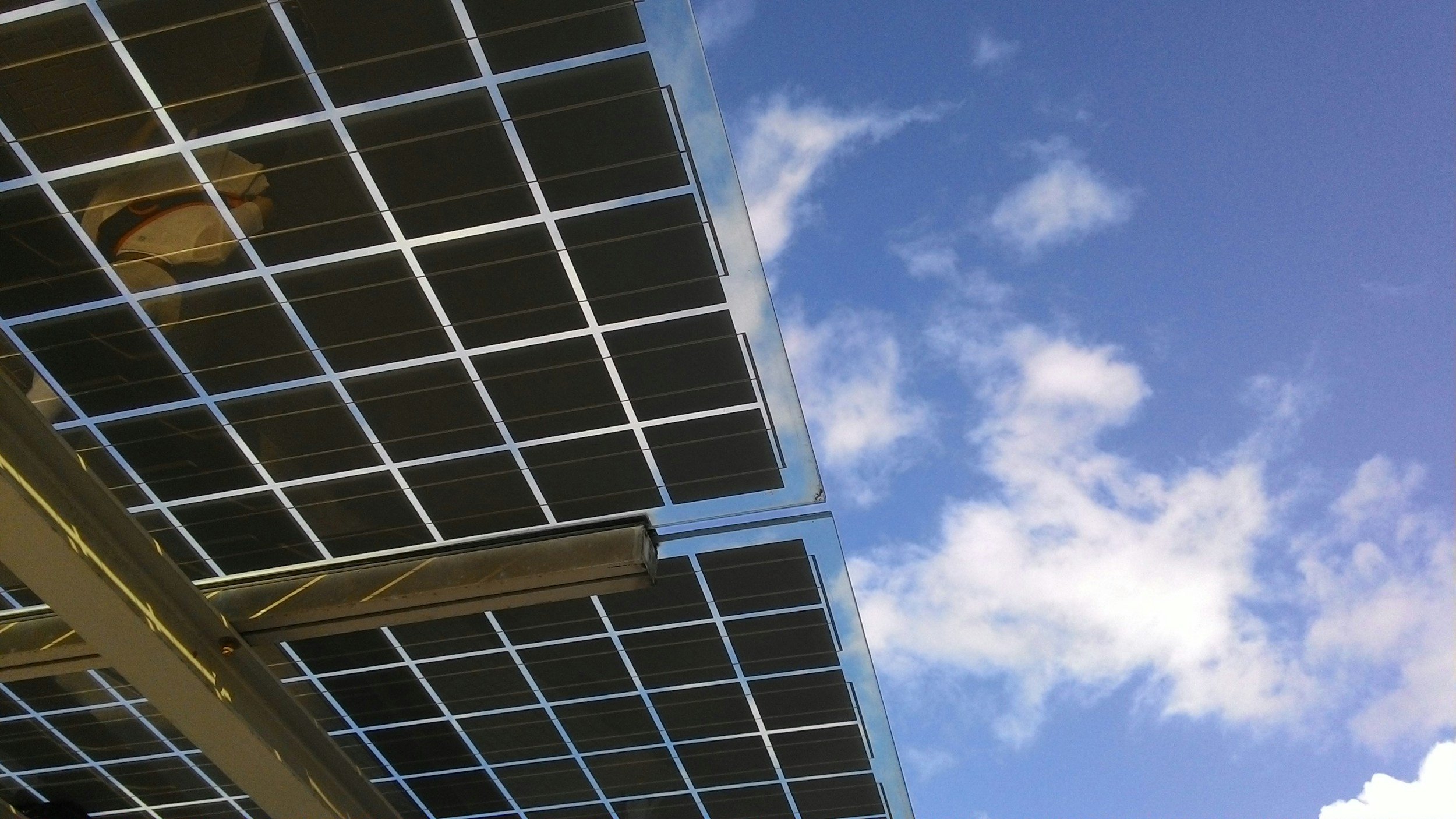Solar panels installed on a building with a blue sky and scattered white clouds in the background.