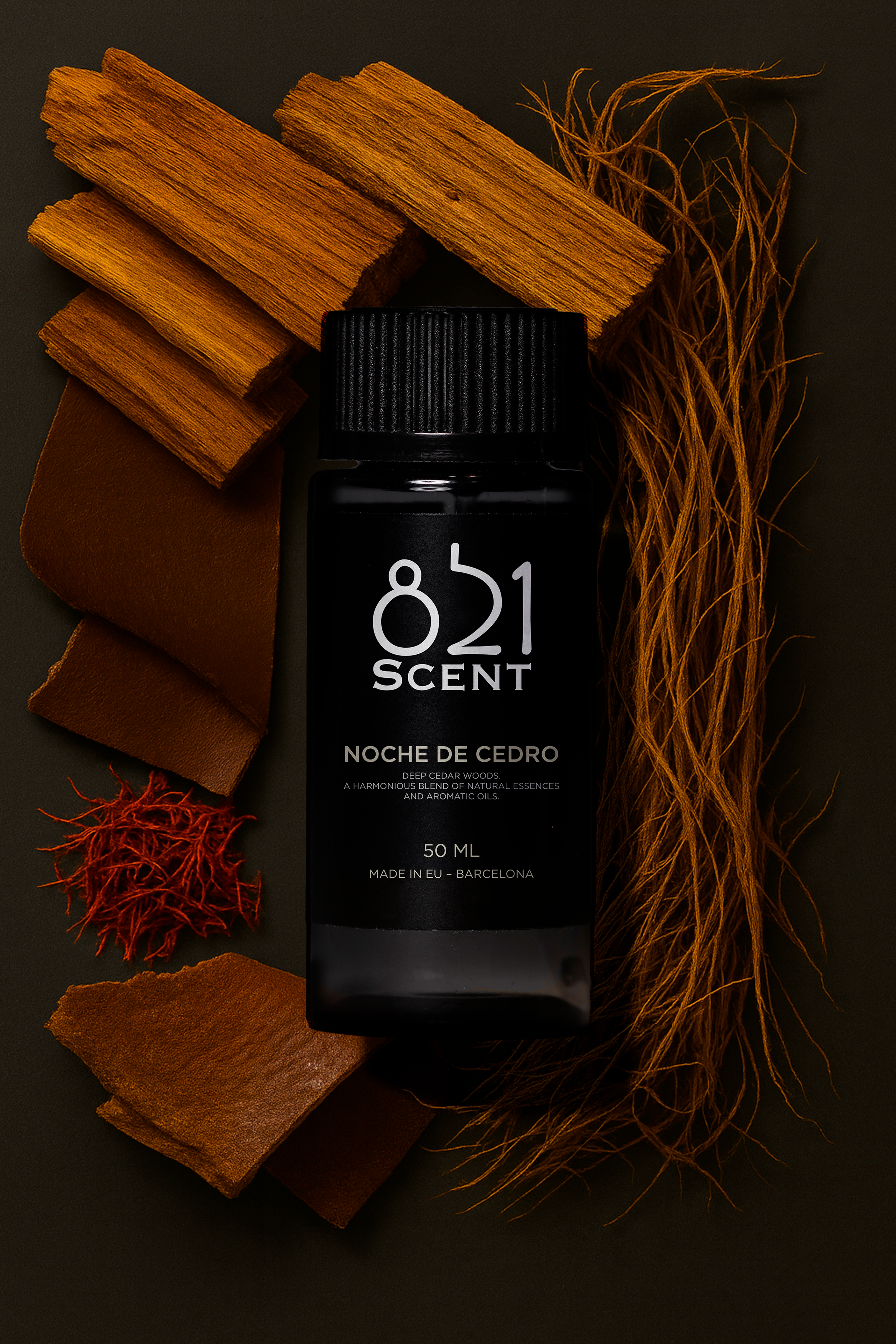 A black bottle labeled '821 Scent' surrounded by cinnamon sticks, leather pieces, red sacha hemp, and dried roots on a dark background.