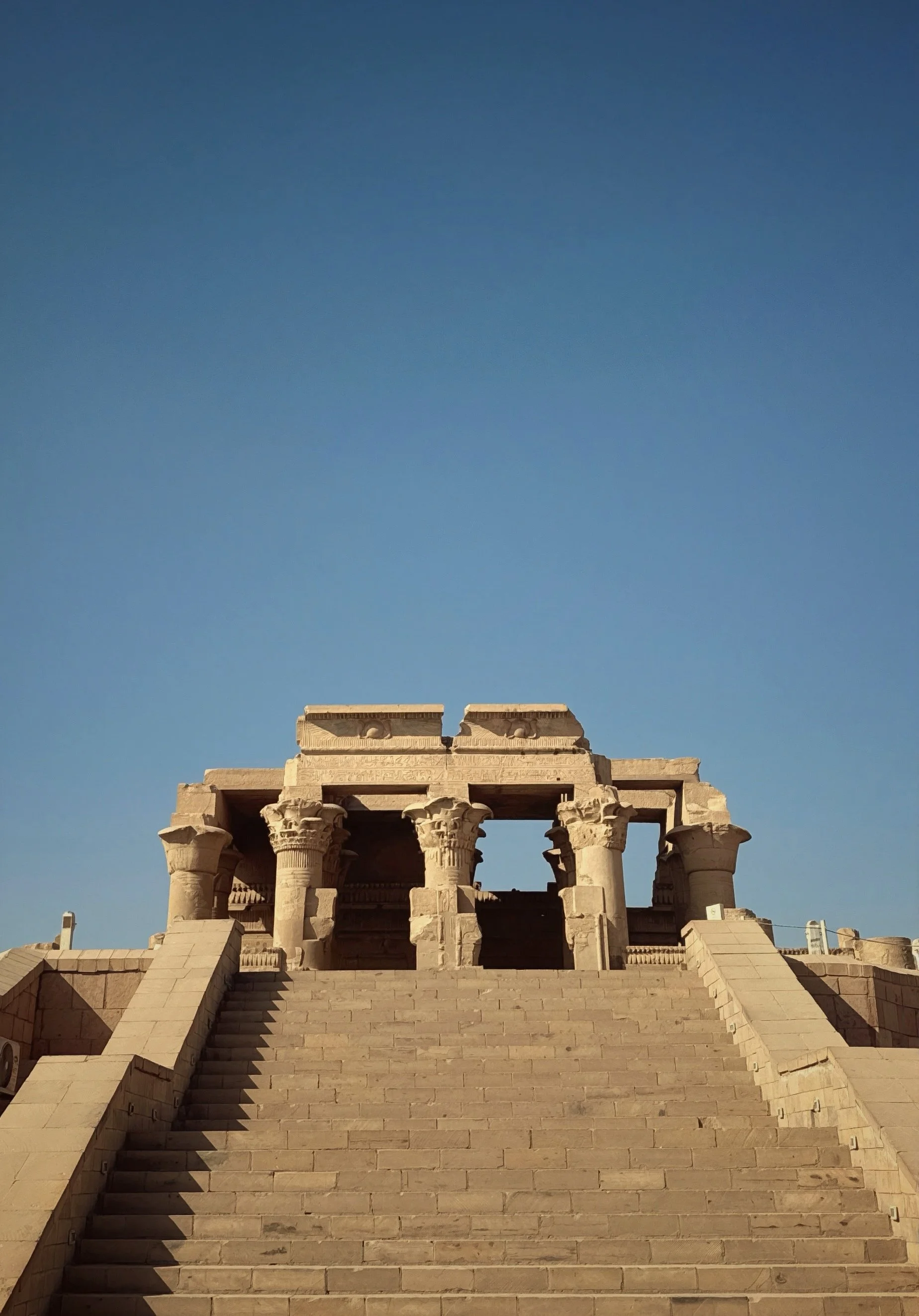 Stone steps leading up to an ancient temple with columns, under a clear blue sky.