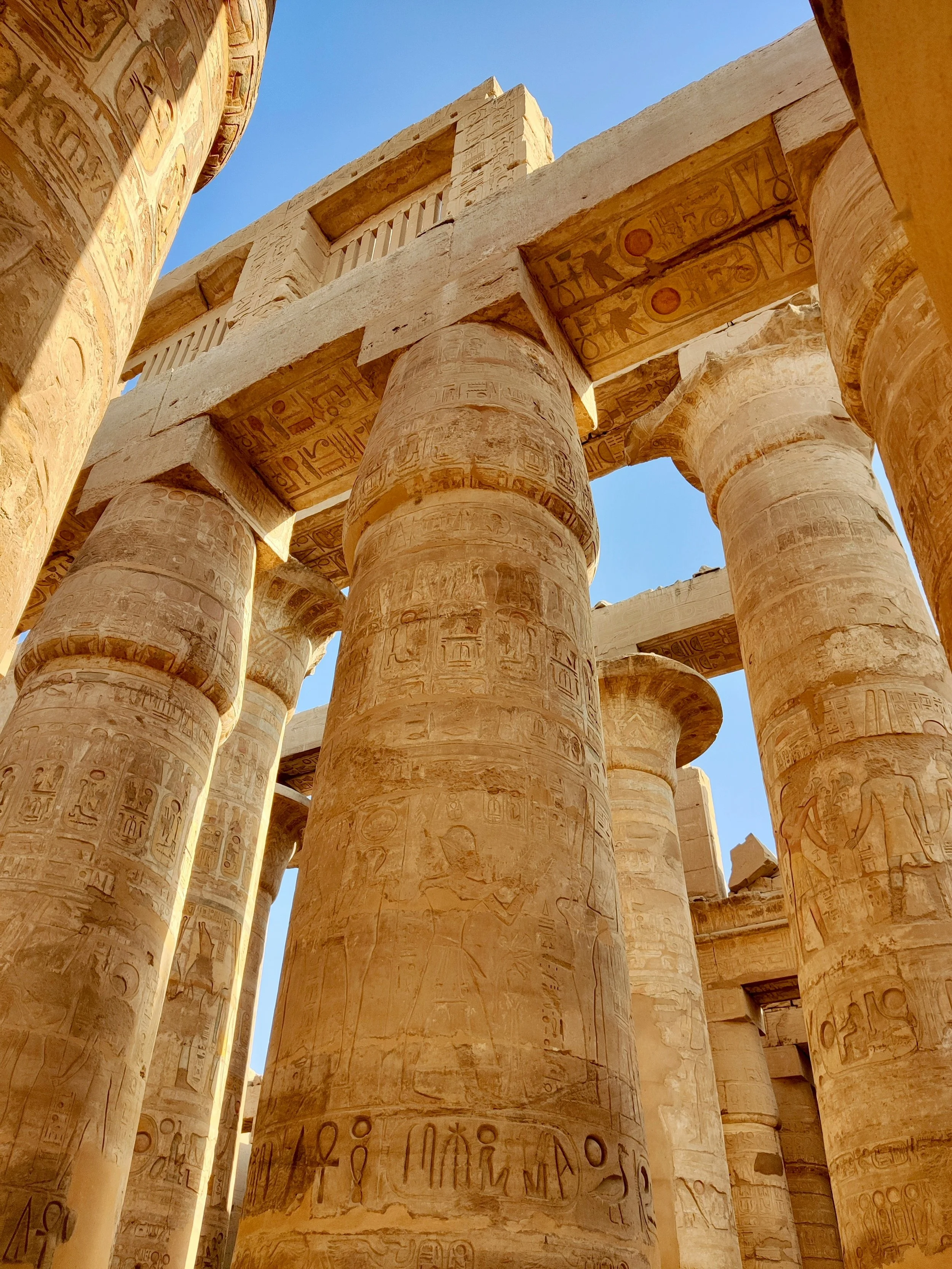 Close-up of ancient Egyptian stone columns with hieroglyphic carvings, part of a temple structure, under a clear blue sky.