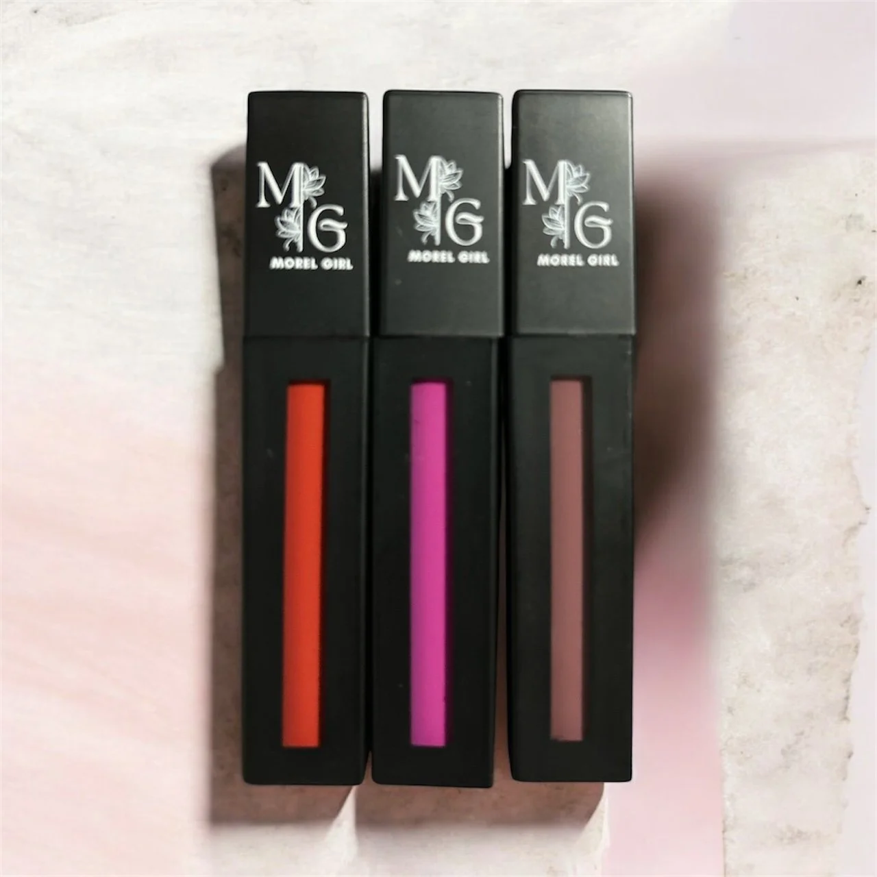 Three lip gloss tubes labeled Morel Girl, with red, pink, and nude shades.