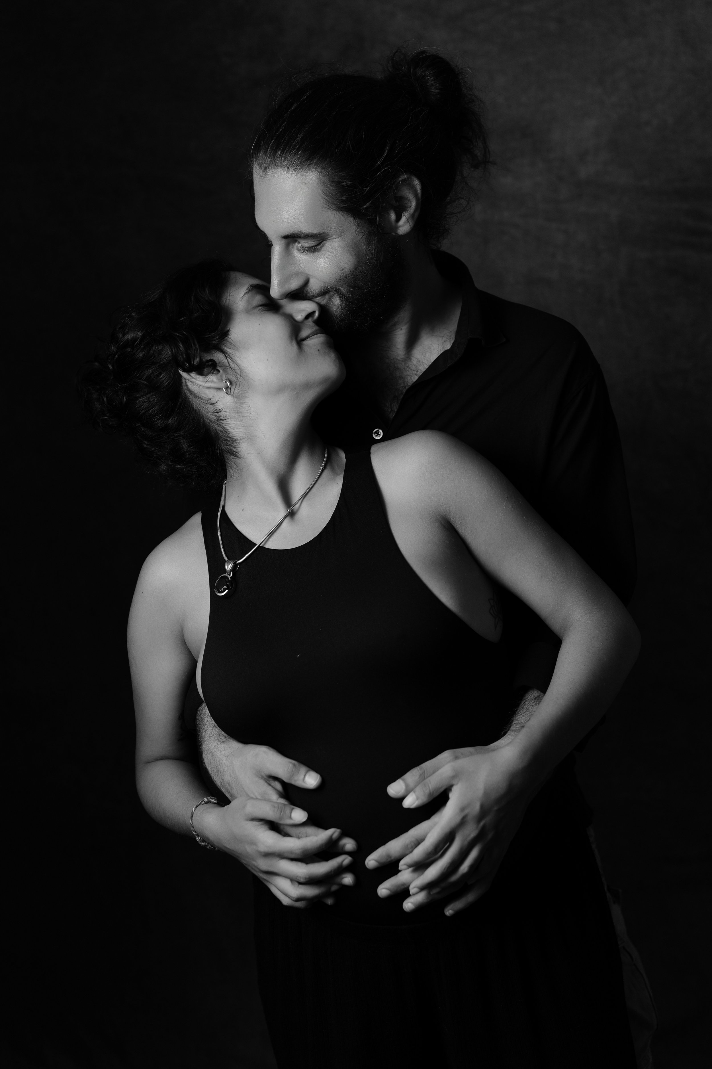 Una coppia si abbraccia, la donna incinta, con sfondo scuro