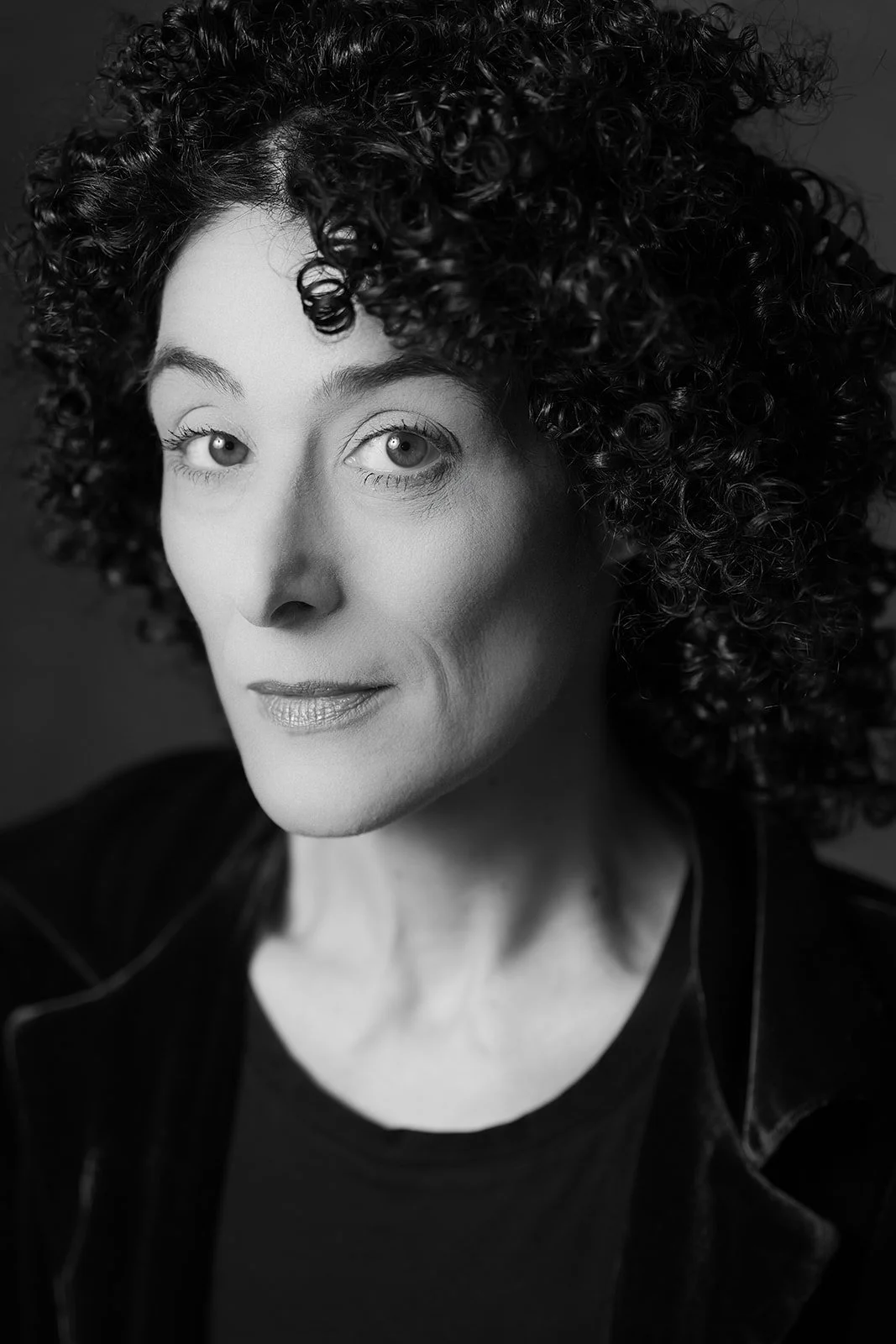 Ritratto in bianco e nero di una donna con capelli ricci e viso serio, sguardo diretto.