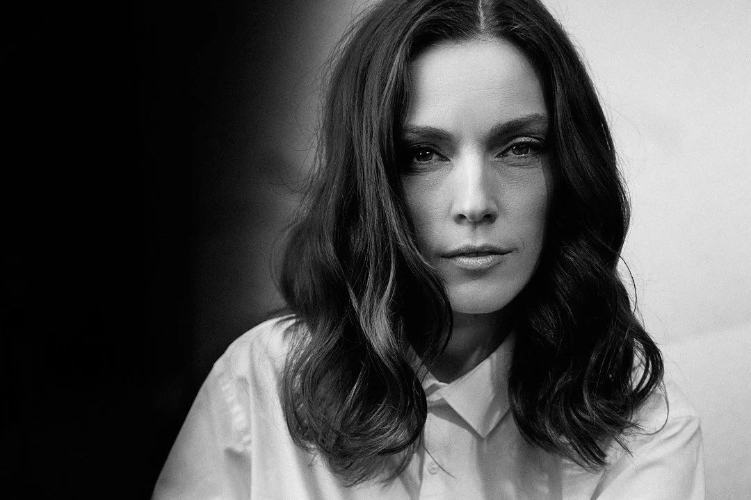 Ritratto di una donna con capelli ricci castani, abbigliamento bianco, in un primo piano in bianco e nero.