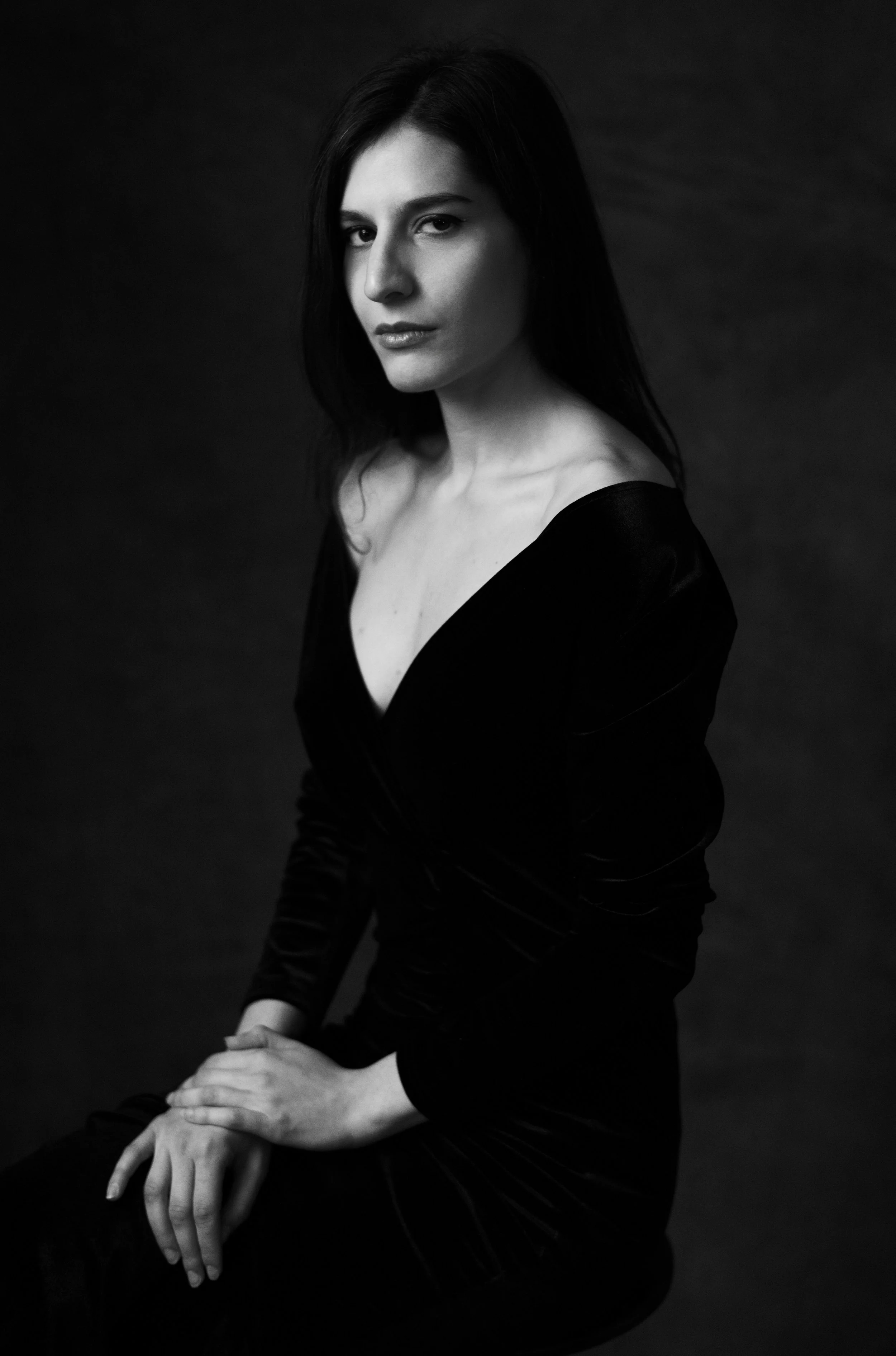 Ritratto in bianco e nero di una donna con capelli scuri, vestita di nero, che guarda verso l'obiettivo con un'espressione seria, seduta contro uno sfondo scuro.