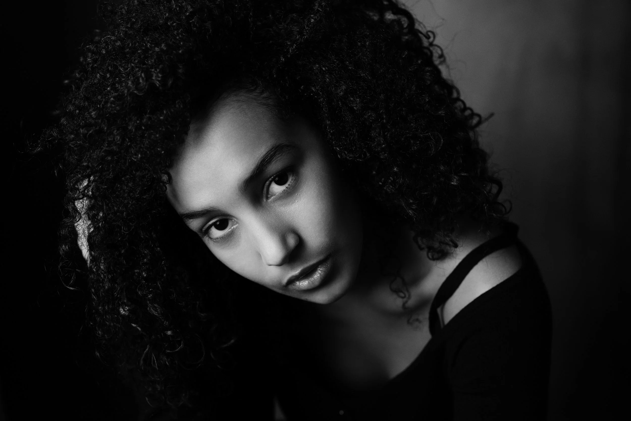 Ritratto in bianco e nero di una giovane donna con capelli ricci, che guarda direttamente l'obiettivo con un'espressione seria.