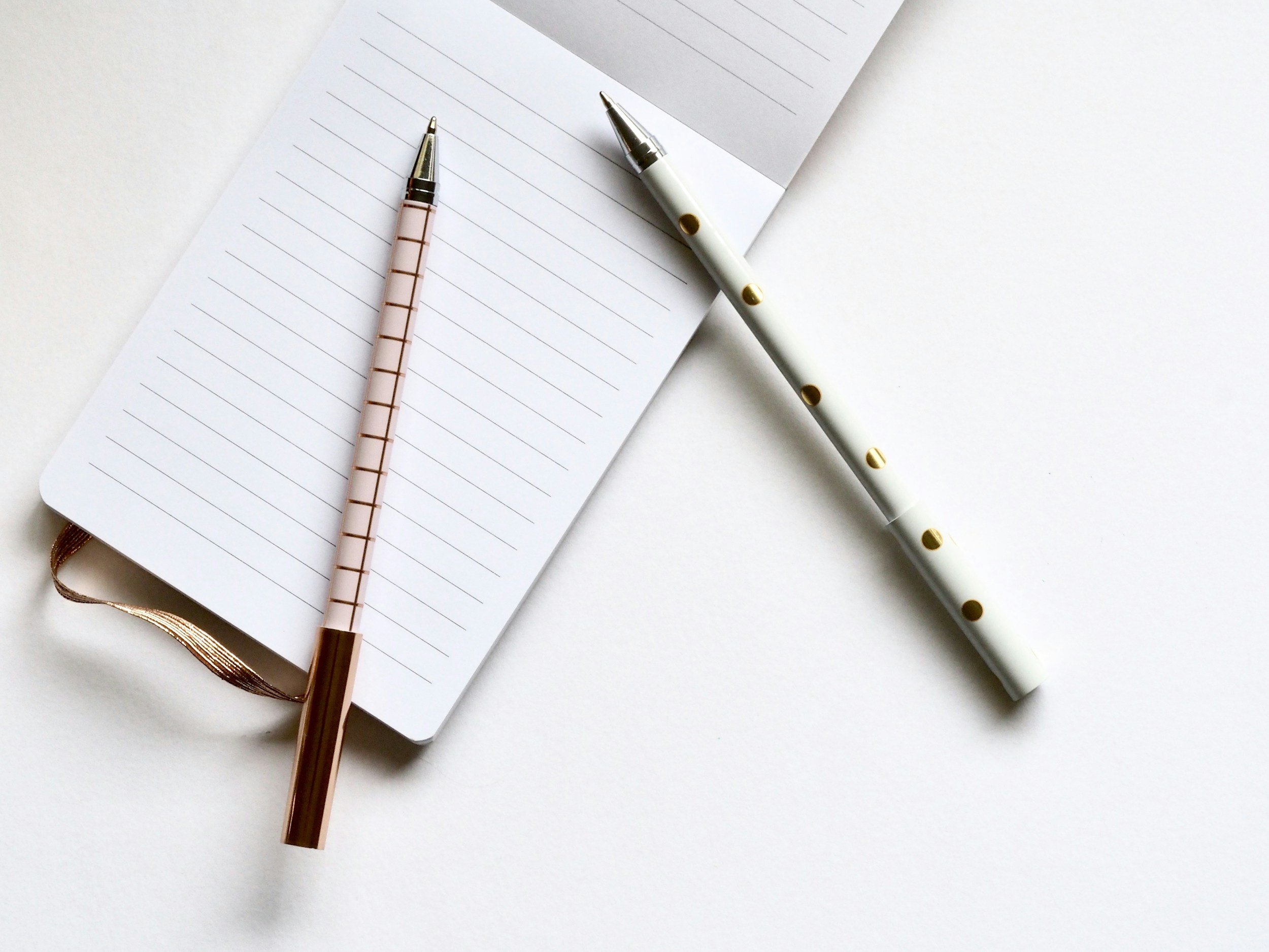 Open lined notebook with two pens on a white surface