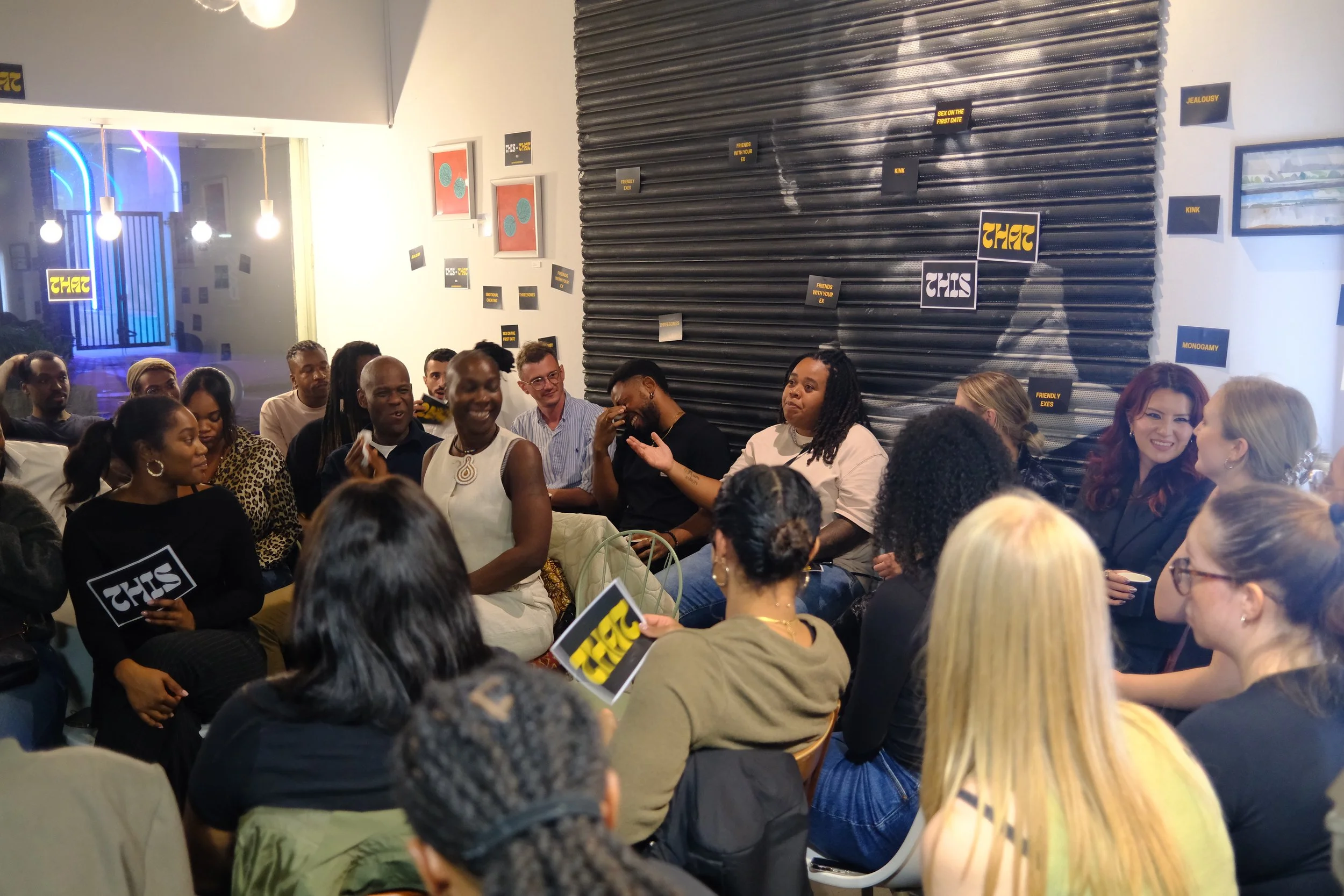 A group of diverse people sitting and engaging in a discussion or panel in a cozy, stylish room with decorative signs on the walls.