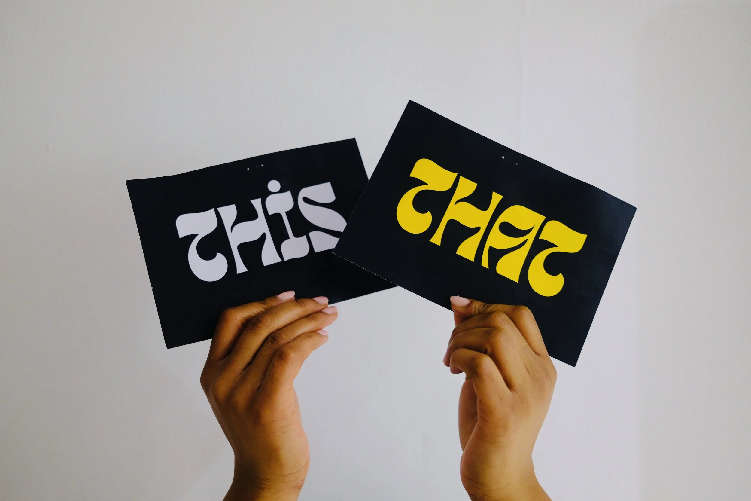 Two hands holding black signs that read "THIS" and "THAT" in opposite orientations.