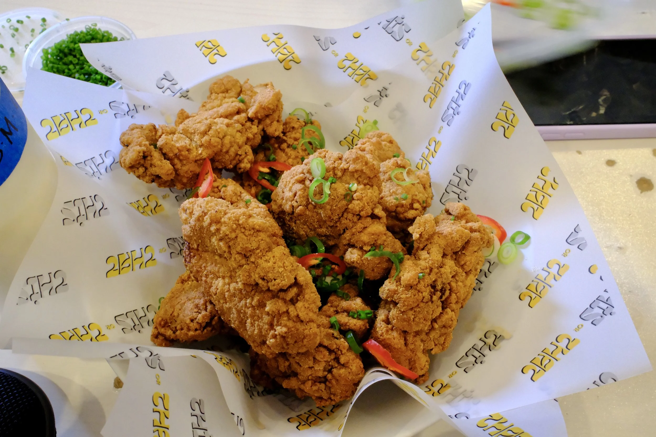 Basket of fried chicken pieces garnished with green onions on branded paper.