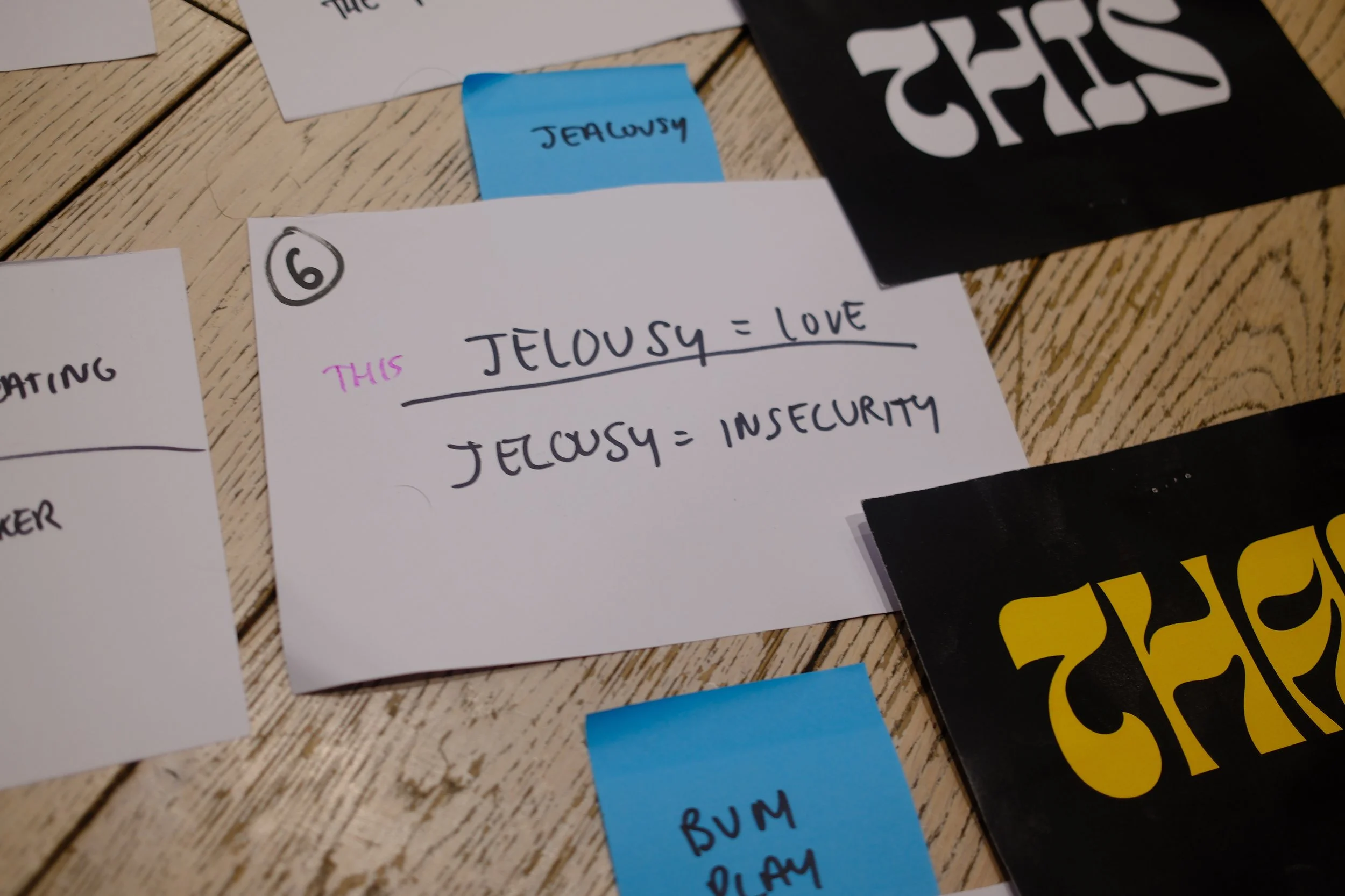 A white card with handwritten text: 'Jelousy = Love, Jelousy = Insecurity,' surrounded by colorful sticky notes on a wooden surface.